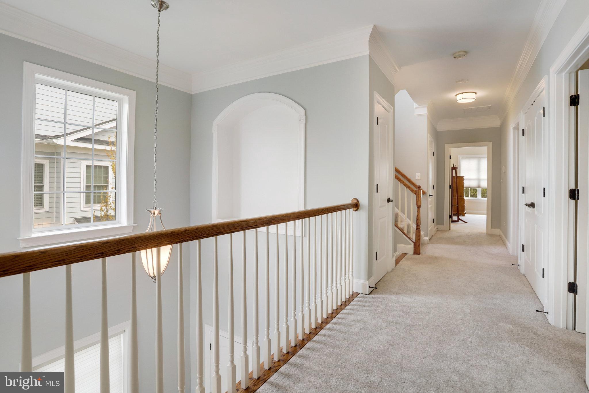 Upstairs hallway with beige carpet, a wood-and-white railing, and a large window overlooking the stairwell.