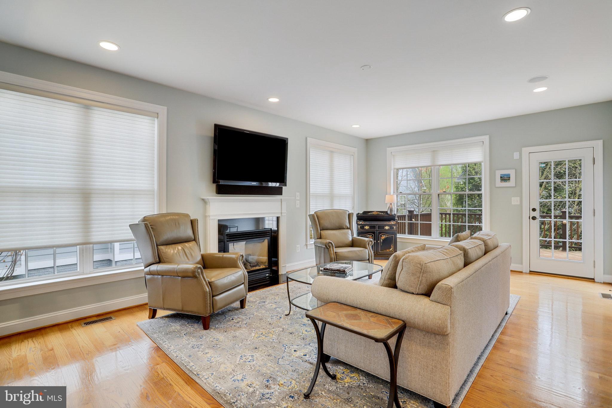 Living room with a fireplace, mounted television, leather armchairs, and large windows.