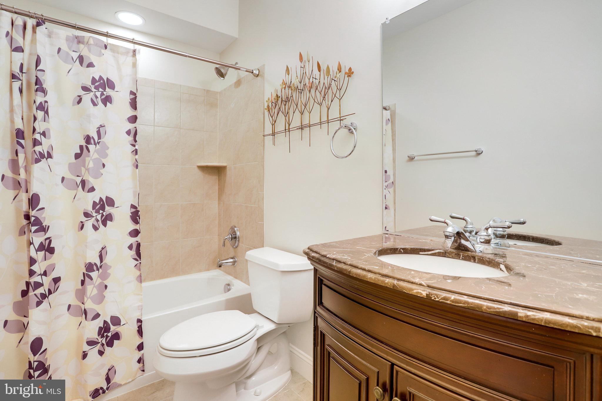 Bathroom with a floral shower curtain, tiled tub surround, and dark wood vanity.