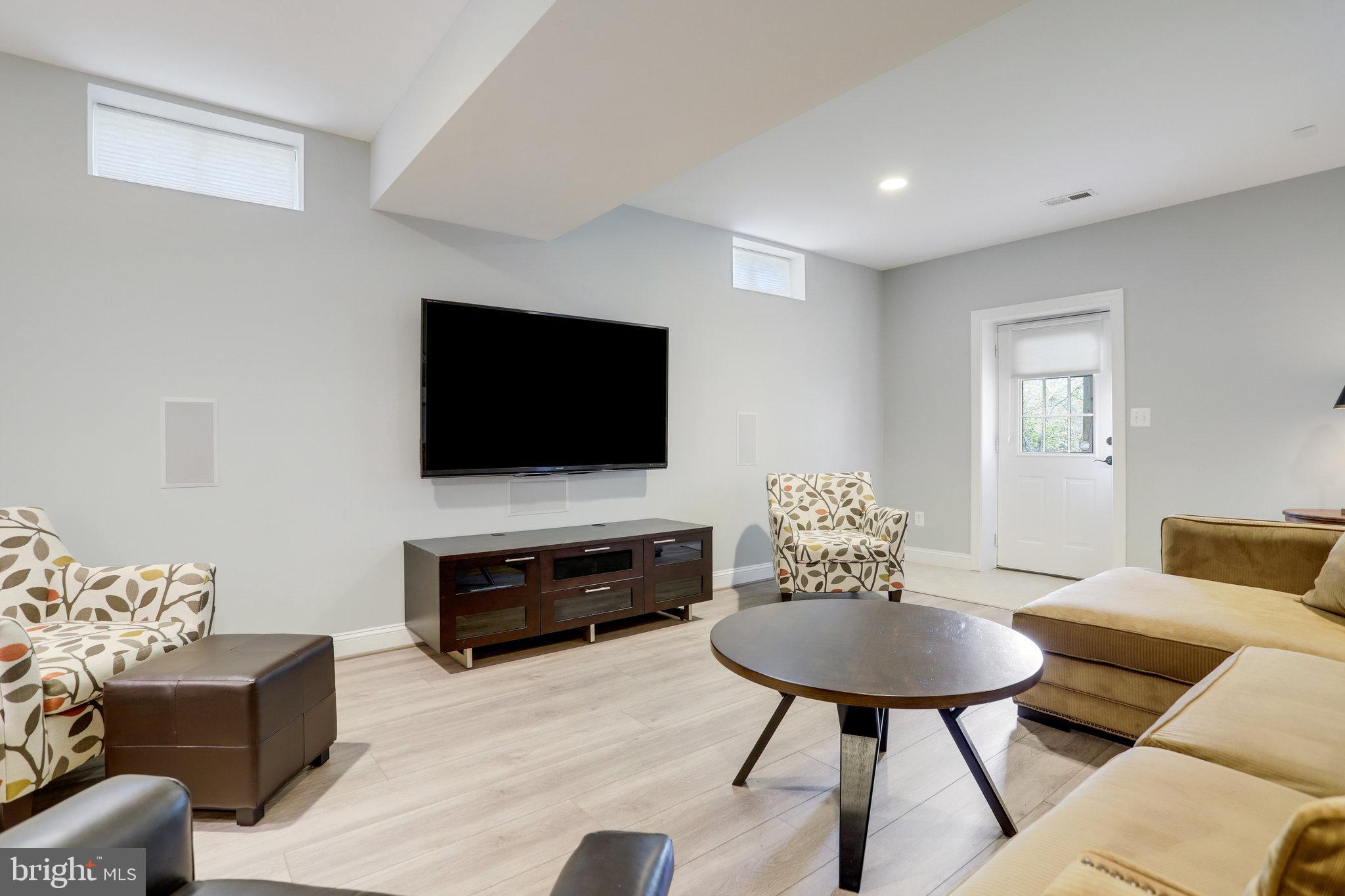 Living room with a wall-mounted TV, patterned armchairs, and a tan sectional.