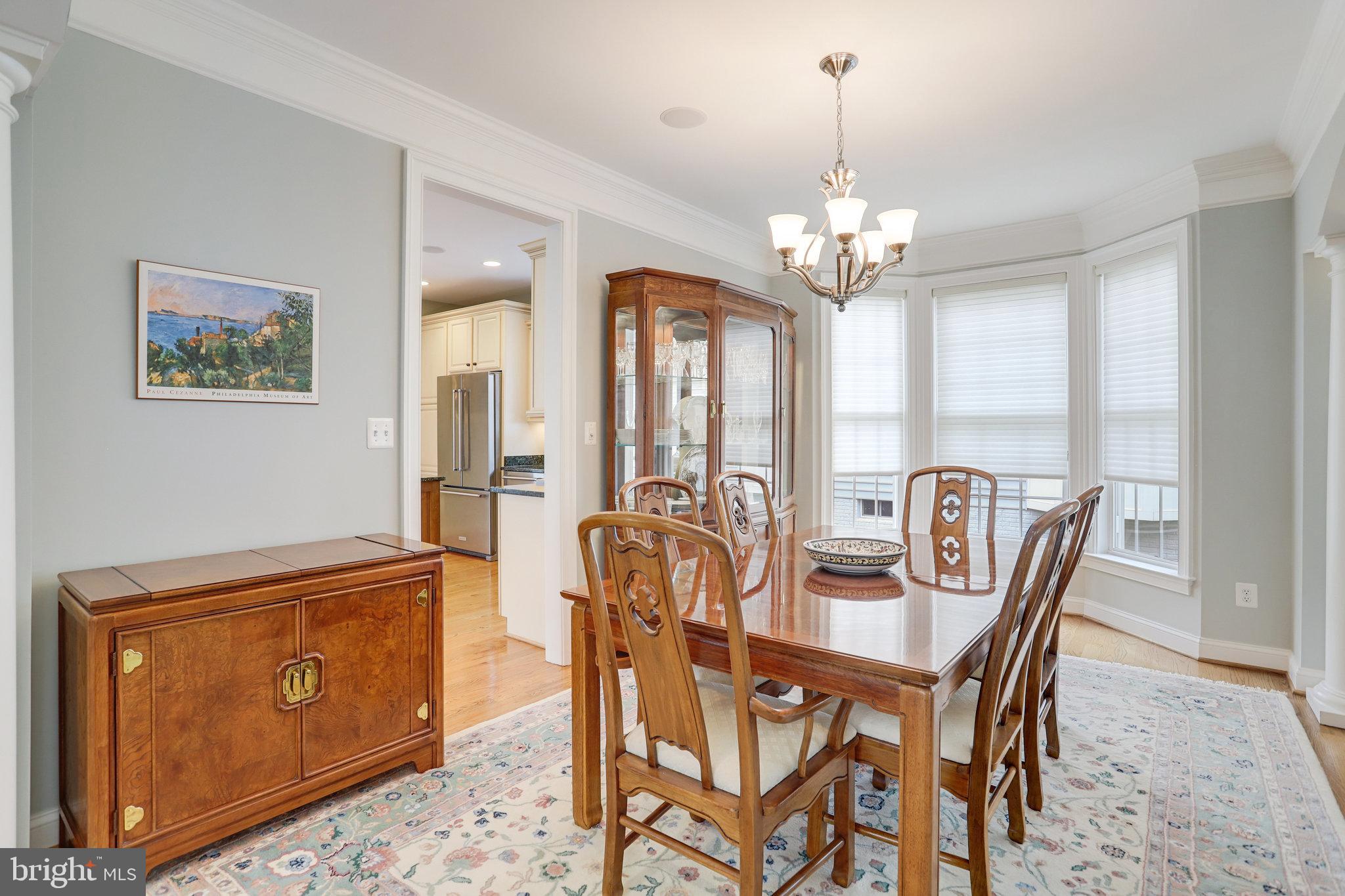 Dining room with a polished wooden table, carved chairs, glass-front china cabinet, and bay windows.
