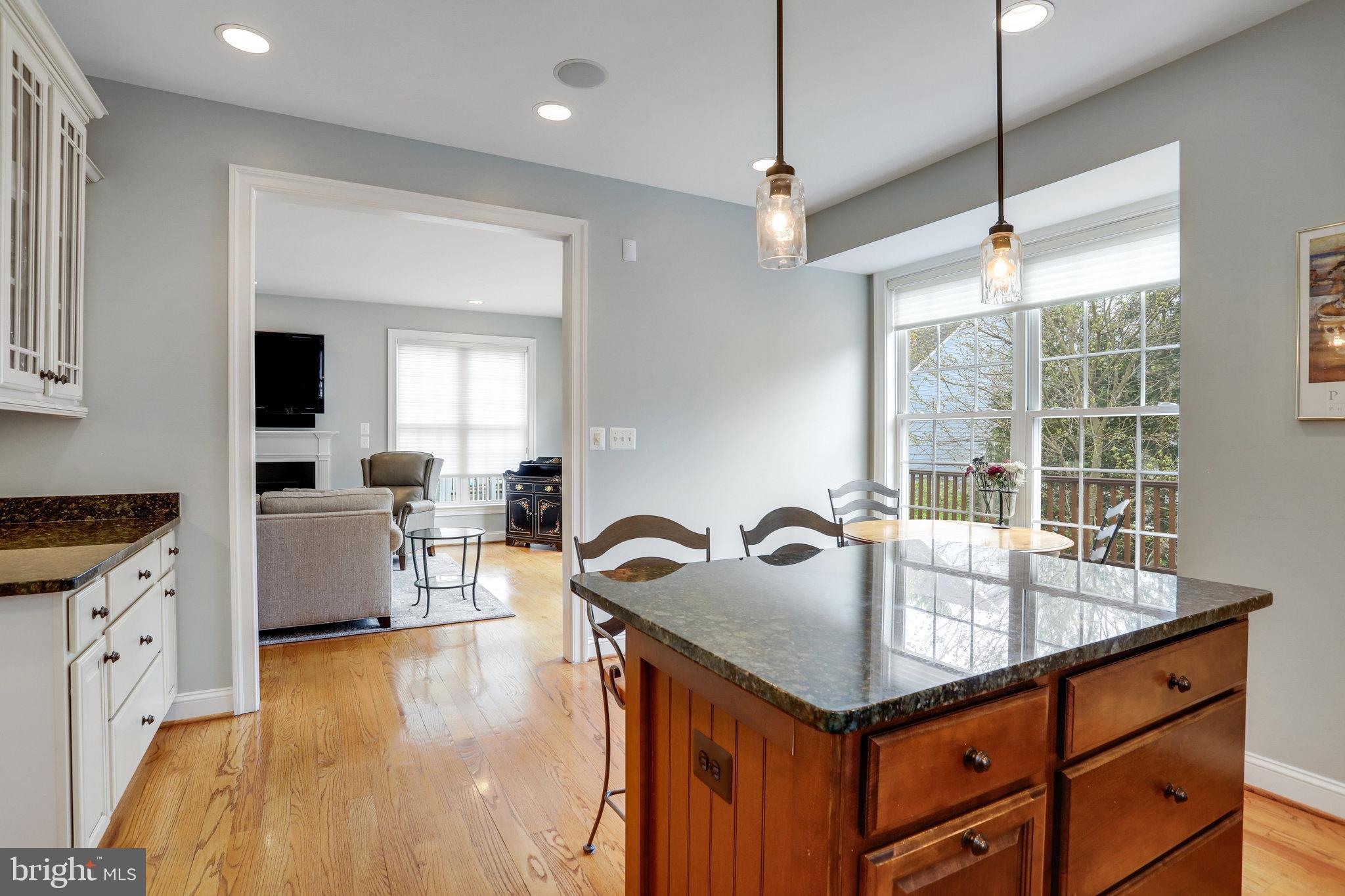 Kitchen and dining area with a large wood island, hardwood floors, and a wide window overlooking trees.