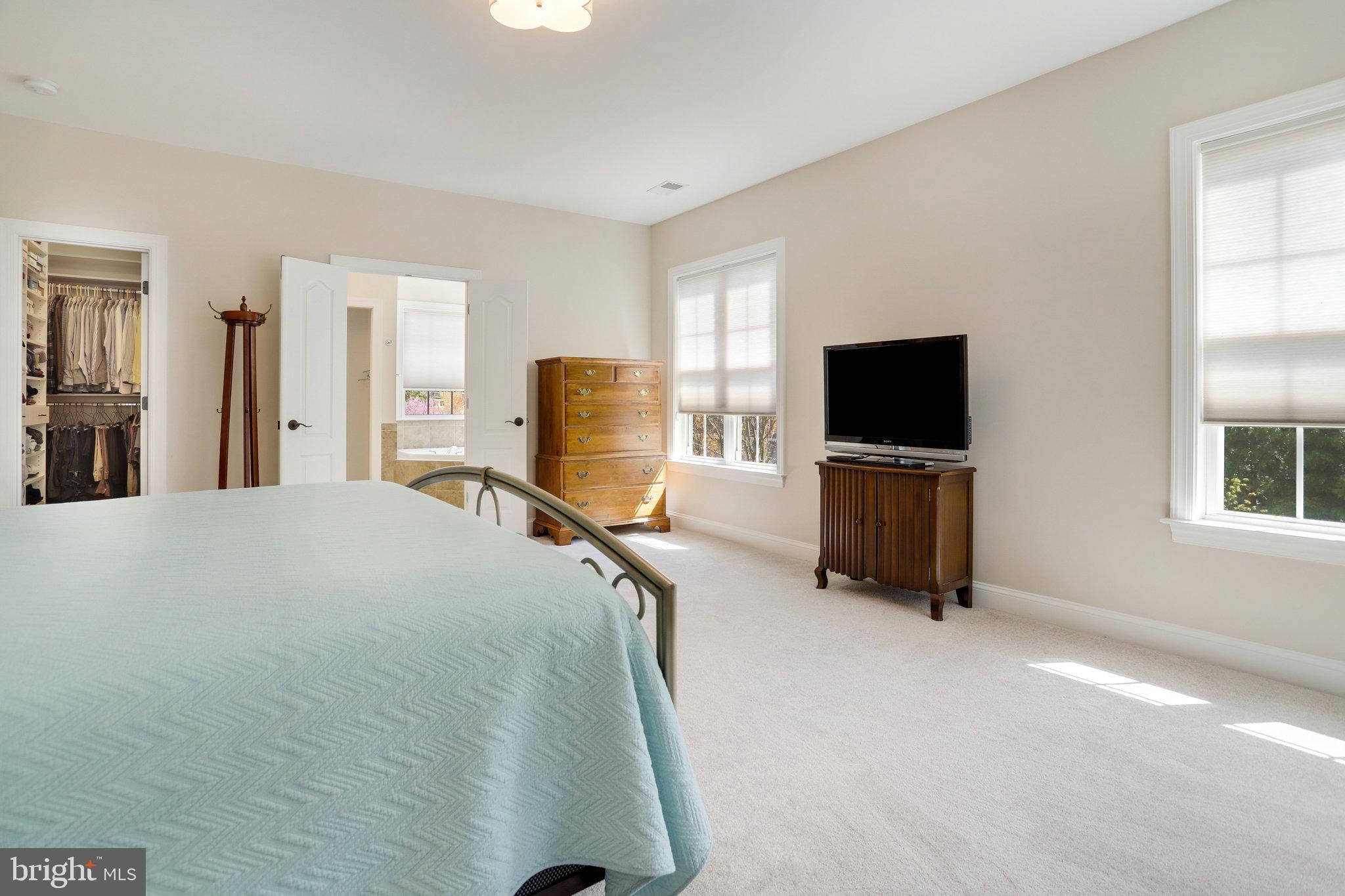Bedroom with an aqua quilted bed, wood furnishings, bright windows, and an open walk-in closet.