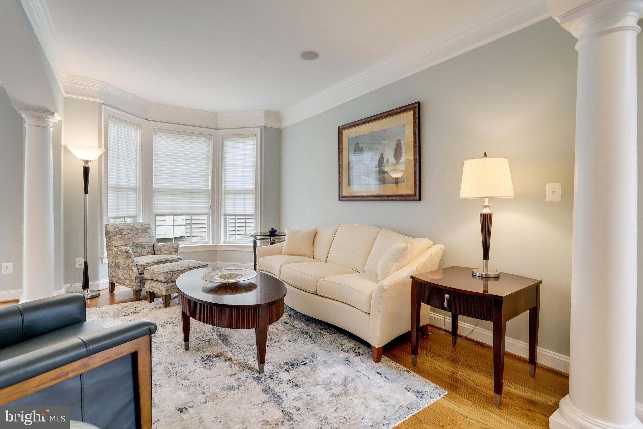 Living room with cream sofa, bay windows, white columns, and dark wood furniture.