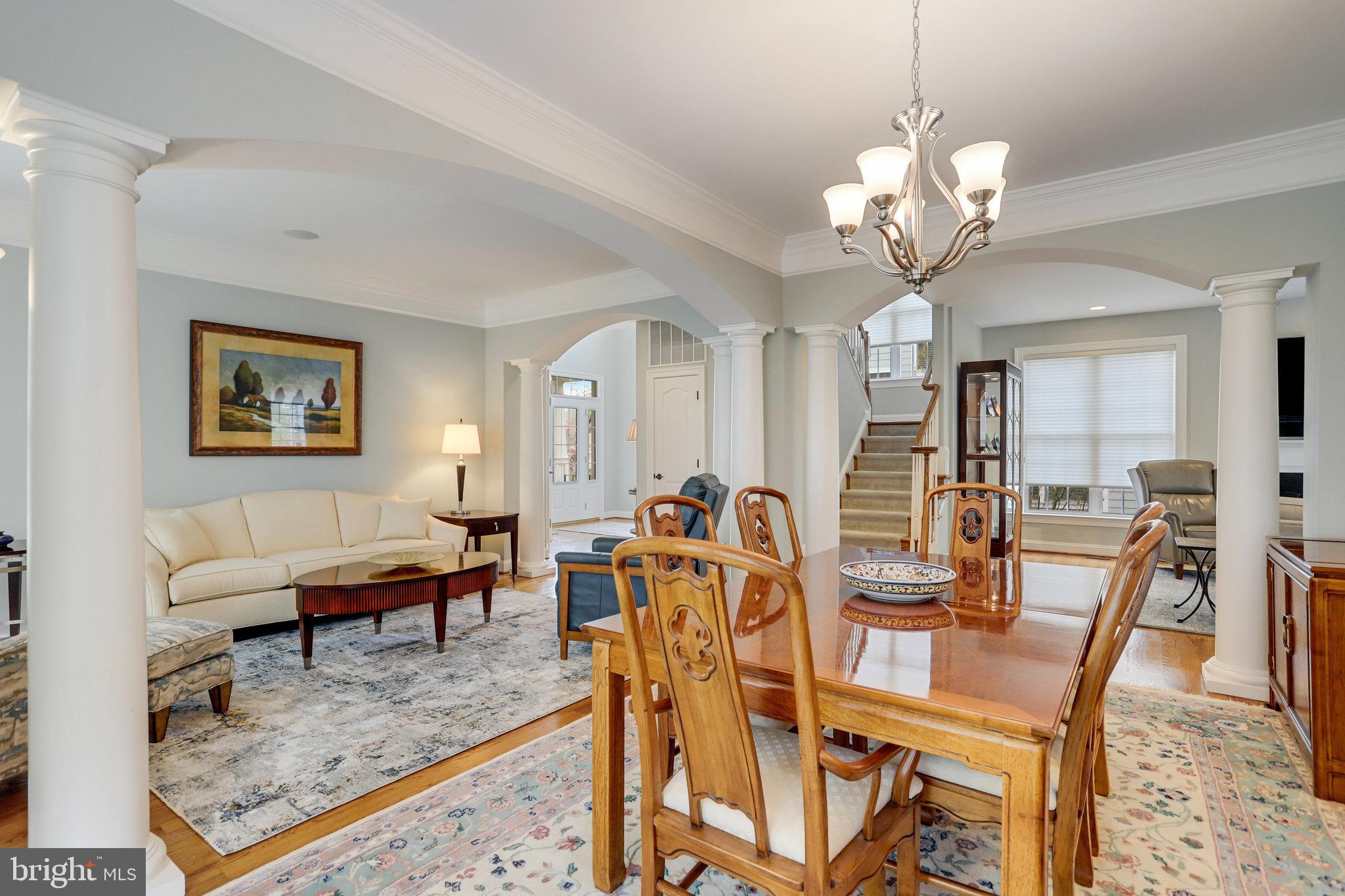 Open-plan living and dining room with carved wood chairs, white columns, and a staircase.