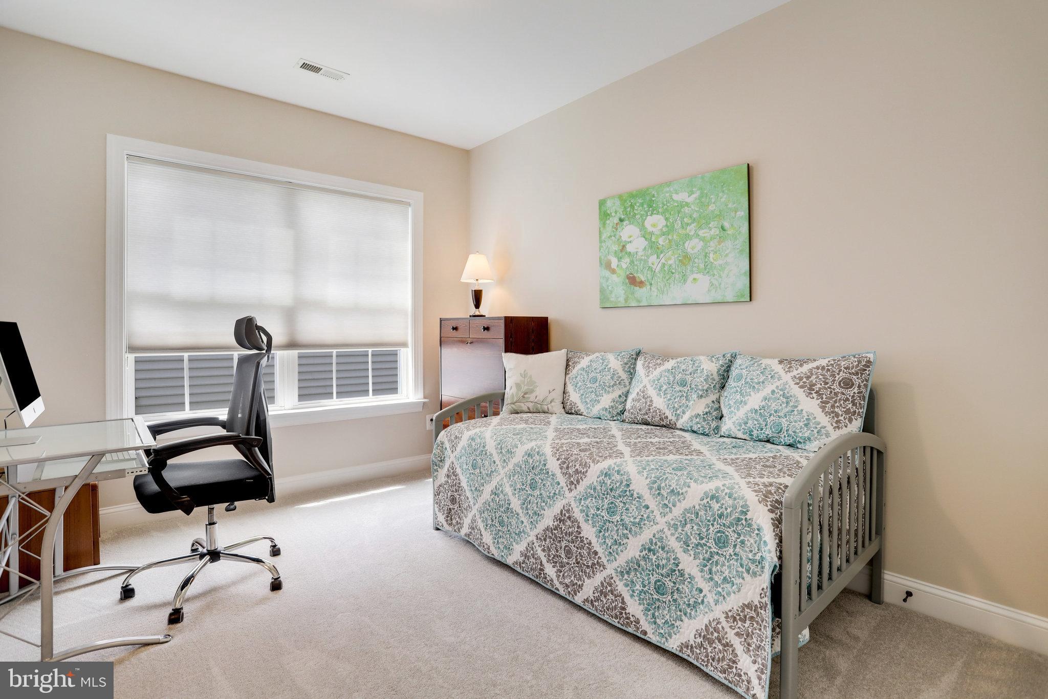 Bedroom with a patterned daybed beside a desk, office chair, and large window.