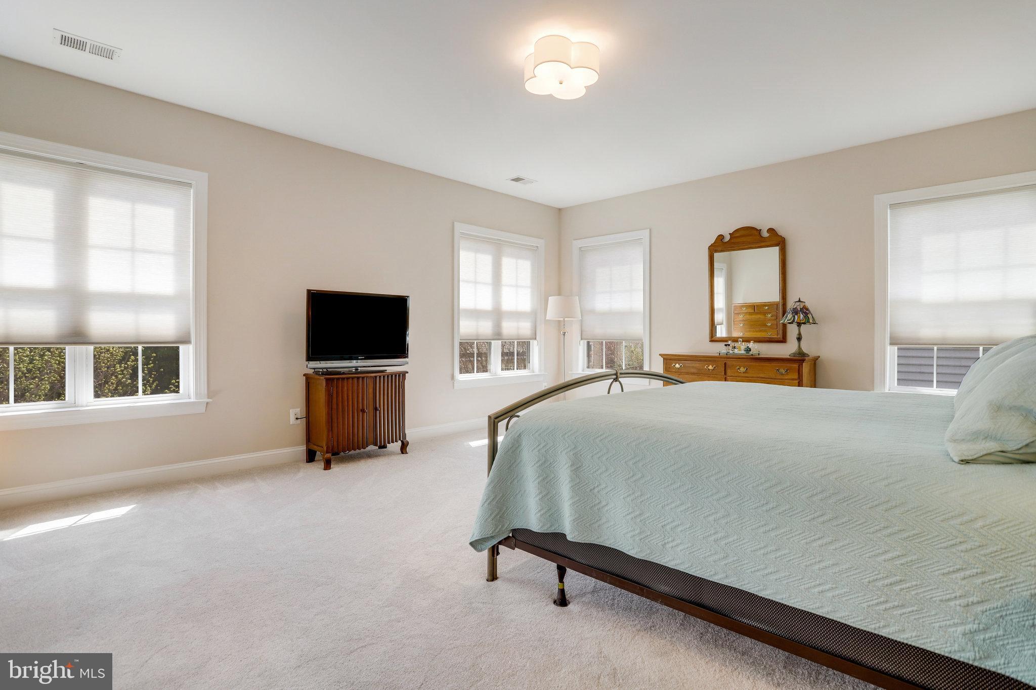 Furnished bedroom with a large pale blue-green bed, multiple windows, and wooden dresser and mirror.