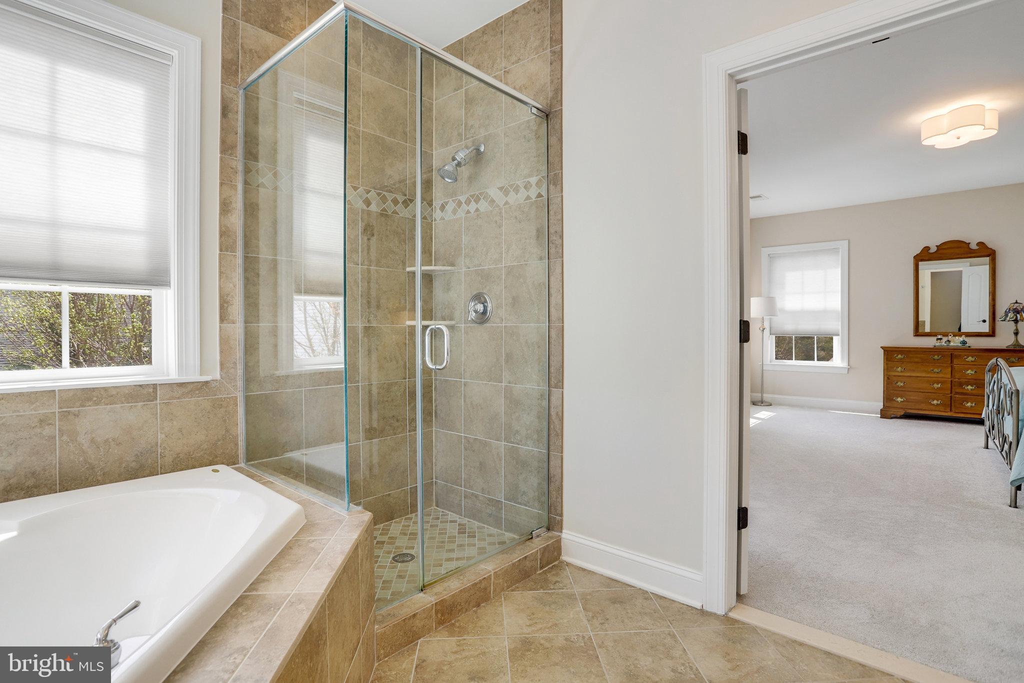 Bathroom with a white soaking tub and glass-enclosed tiled shower beside a bedroom doorway.