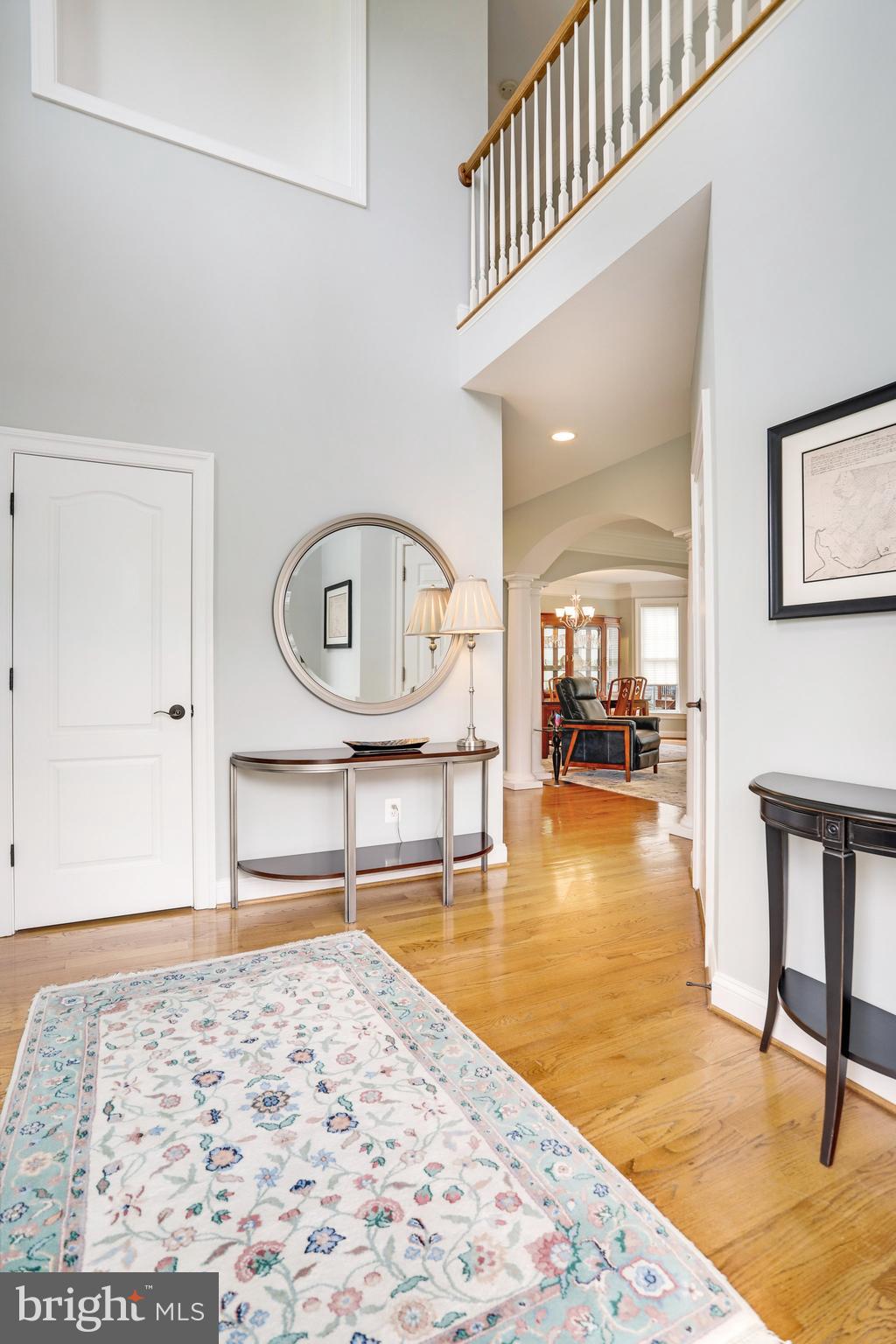 Two-story foyer with hardwood floors, a patterned rug, round mirror, and upper-level railing.