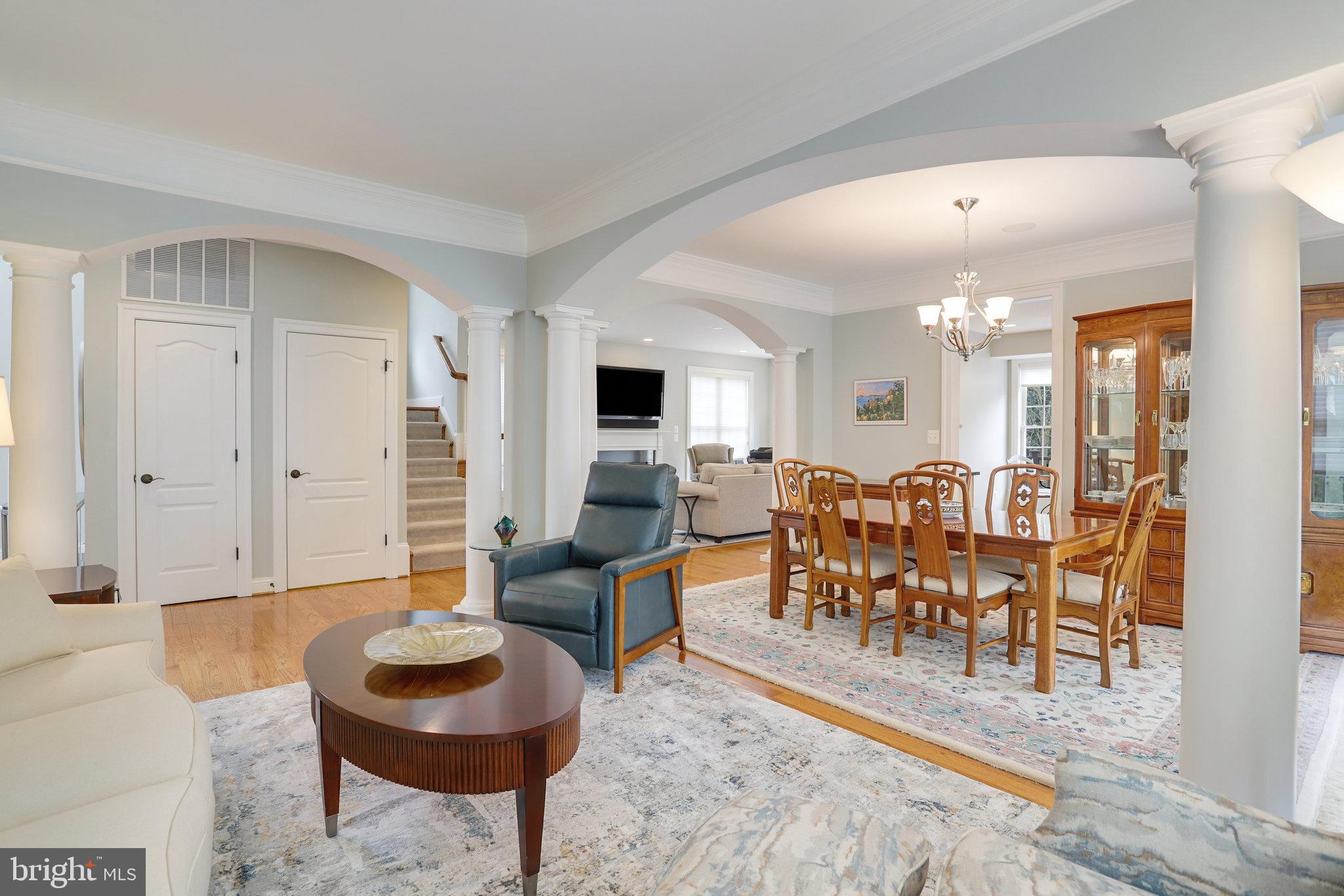 Open-plan living and dining room with white columns, arched openings, and a wooden dining set.