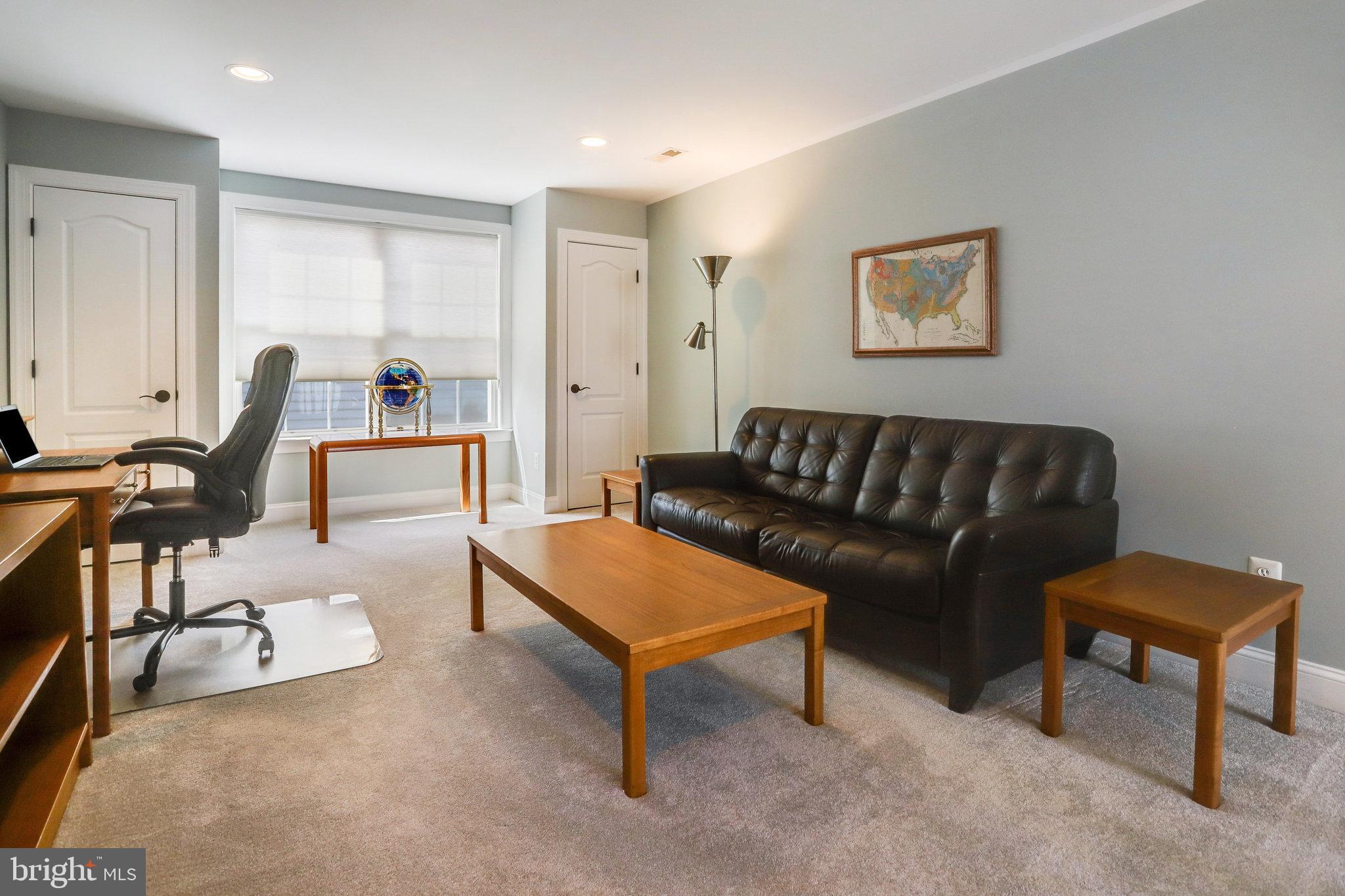 Furnished home office with a leather sofa, wooden tables, desk, and window.