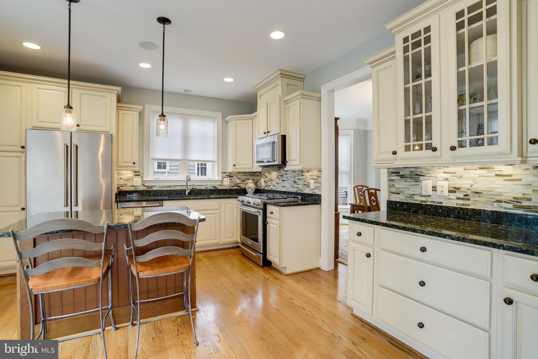 Kitchen with cream cabinets, dark countertops, stainless steel appliances, and a breakfast island with two stools.