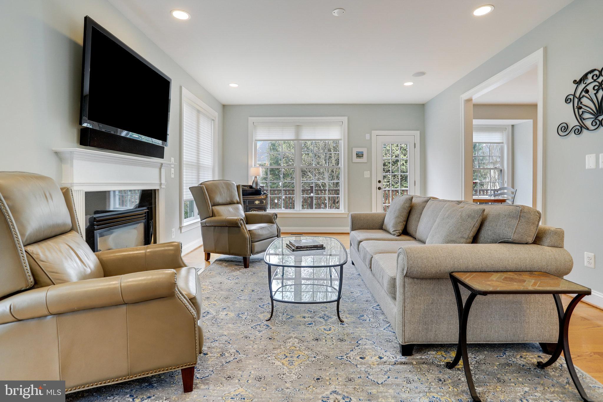 Living room with a gray sofa, tan leather chairs, fireplace, and large windows.