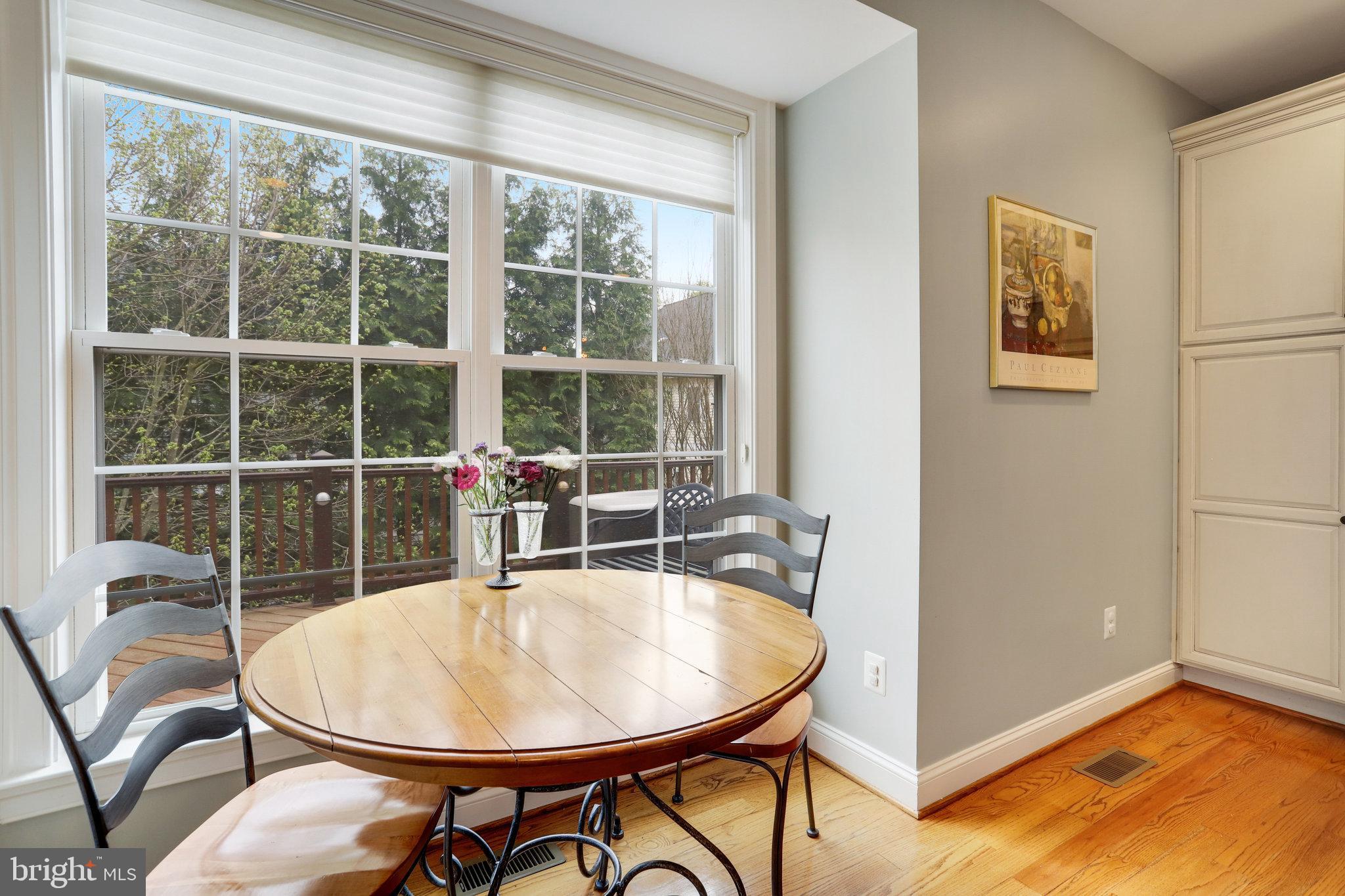 Dining area with an oval wooden table beside large windows overlooking trees and a deck.