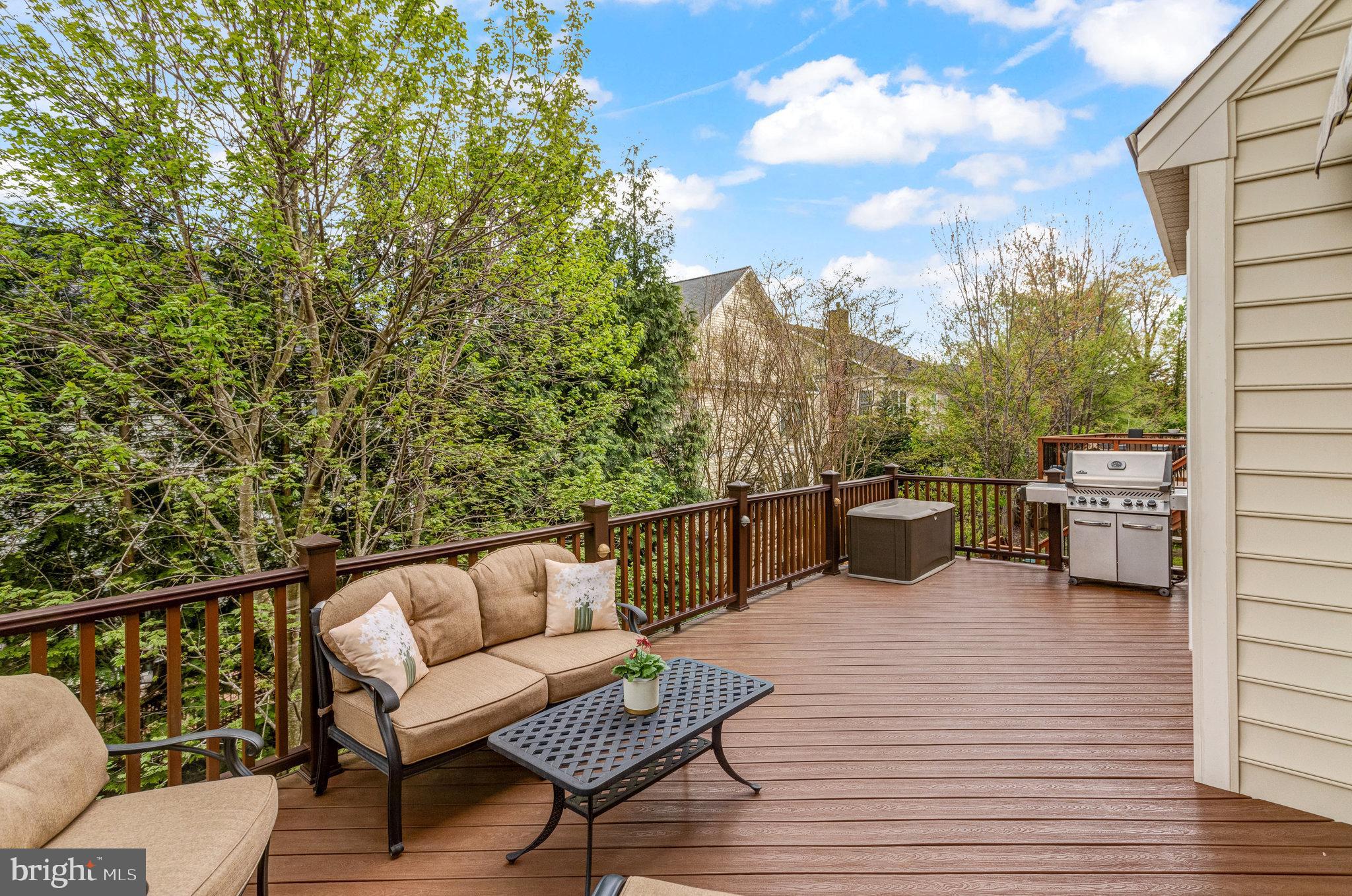 Composite deck with cushioned seating and a grill, overlooking leafy trees.