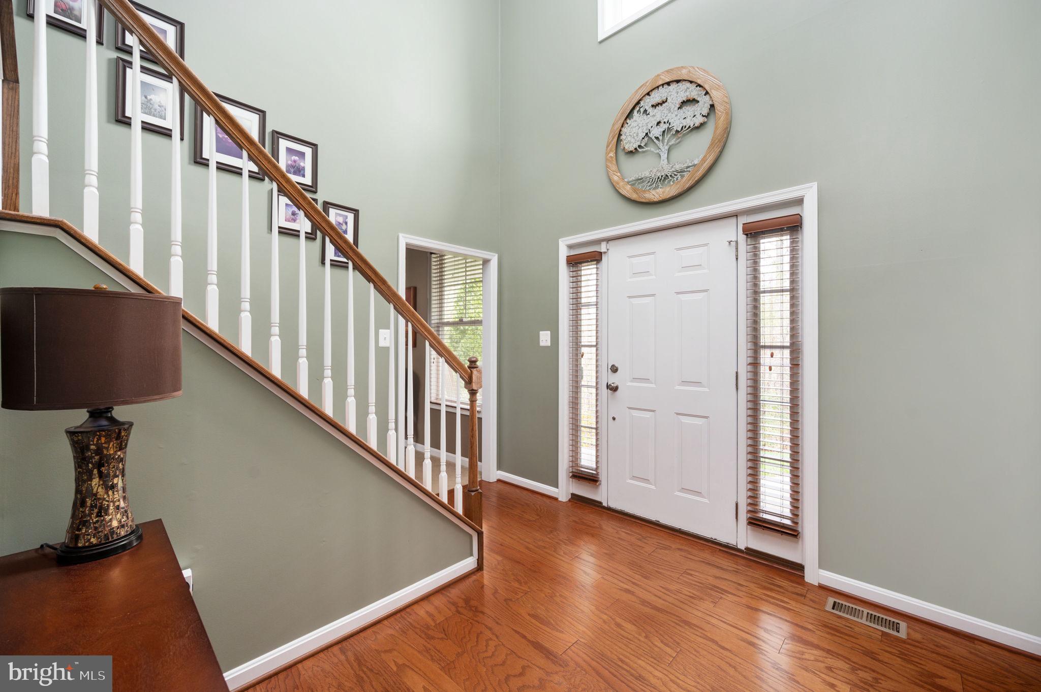 Entry foyer with hardwood floors, a white front door, and a staircase with white balusters.