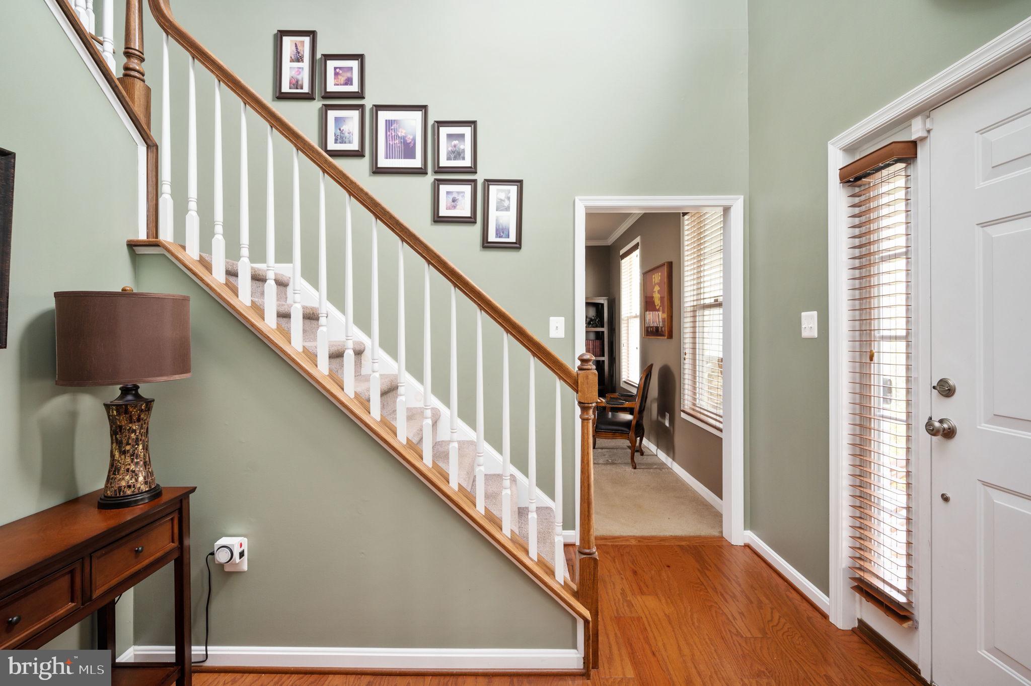 Entry foyer with carpeted staircase, wood handrail, framed pictures, and hardwood floor.