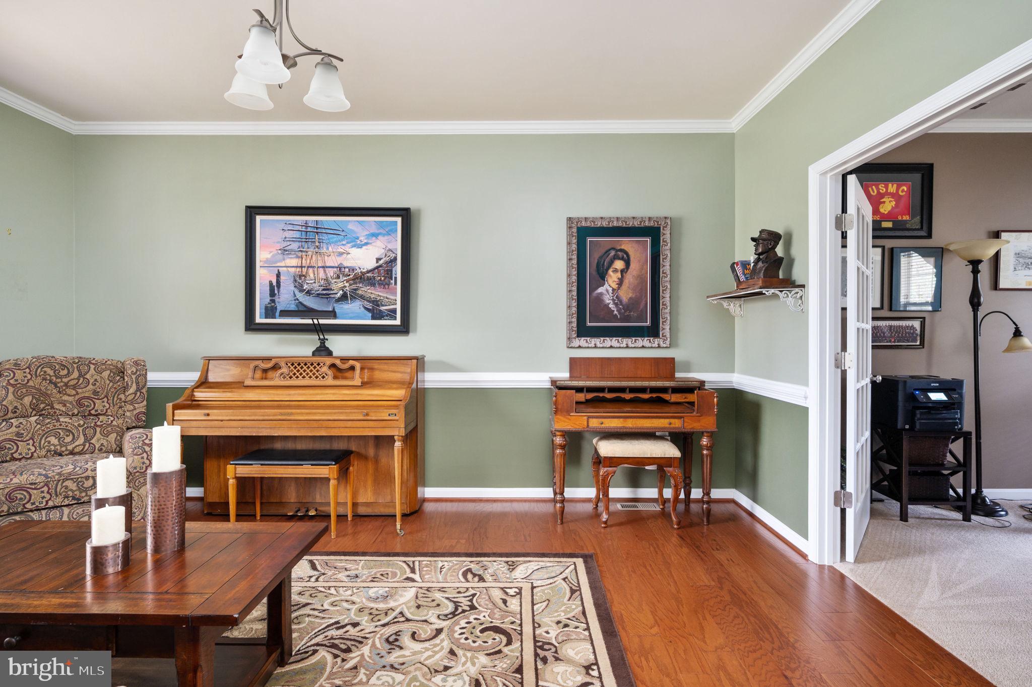 Furnished room with a piano, ornate writing desk, and open doorway to an office.