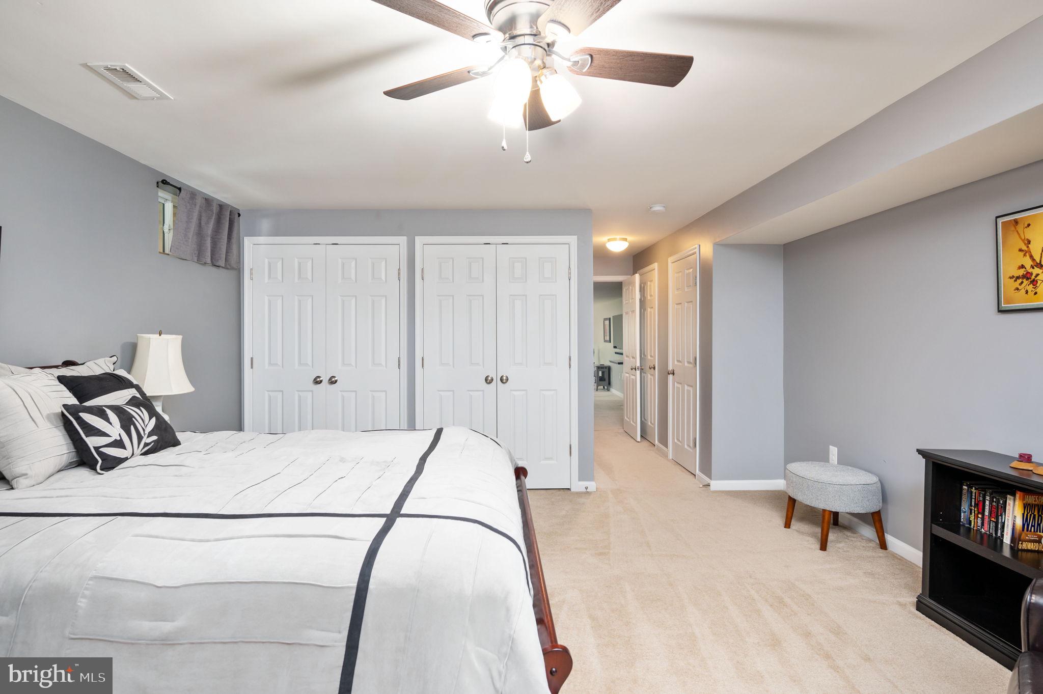 Furnished bedroom with white bedding, double closet doors, and a ceiling fan.
