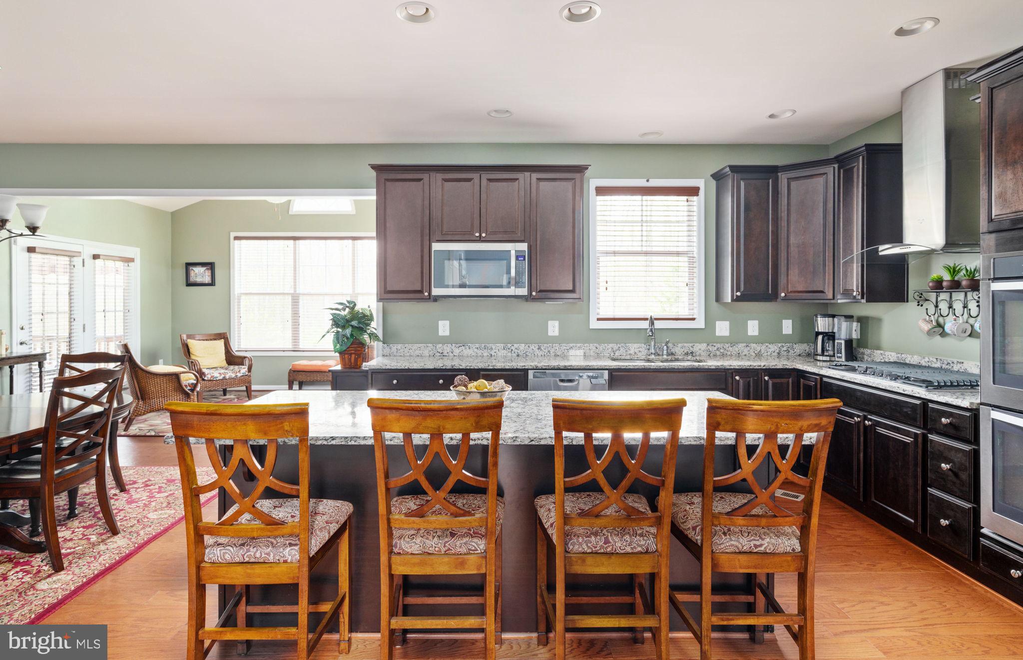 Kitchen with dark wood cabinets, granite counters, and a large island with four bar stools.