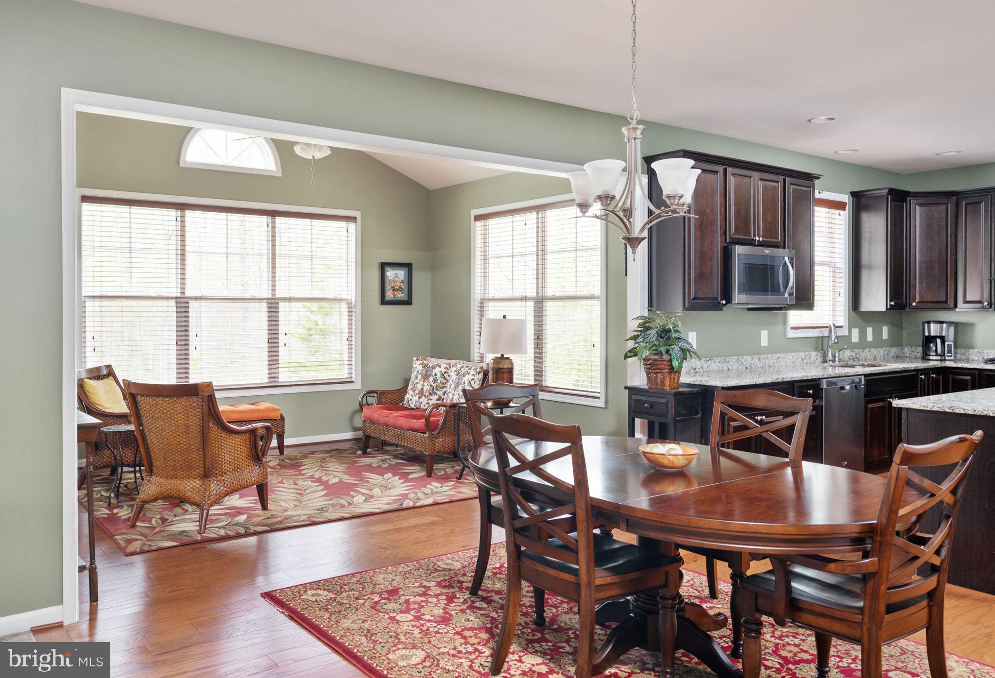 Dining area with a wooden table and chairs beside a furnished sitting nook, opening into a dark-cabinet kitchen.