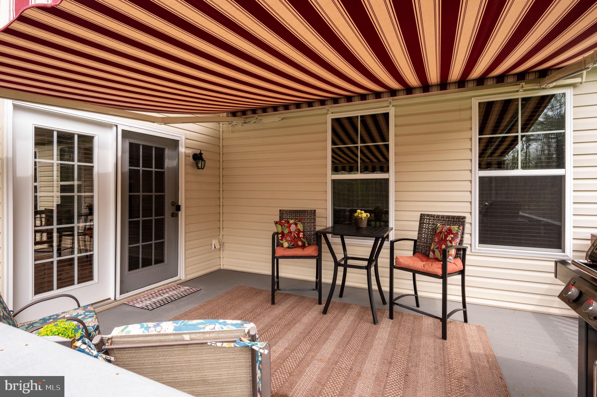 Covered patio with a striped awning, outdoor seating, a small table, and a grill.