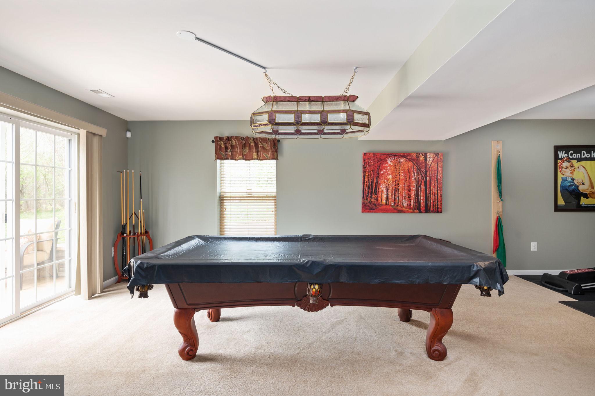 Game room with a covered billiards table, pool cues, and sliding glass doors.