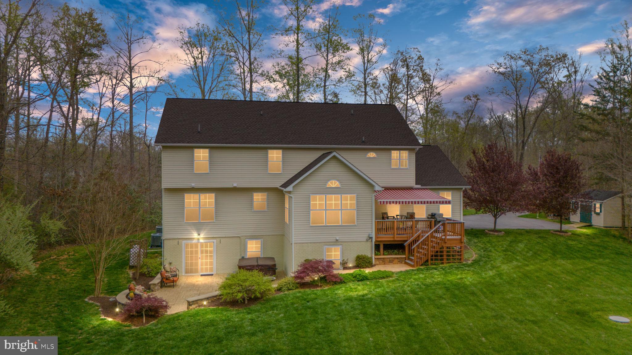 Two-story home with a striped-awning deck and landscaped lawn at dusk.