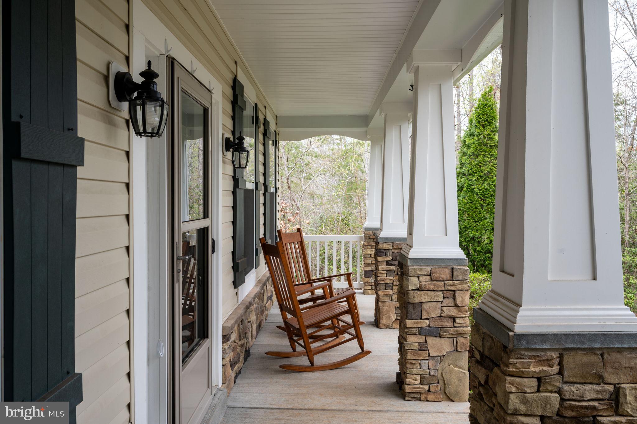 Covered front porch with stone-based columns and two wooden rocking chairs overlooking trees.