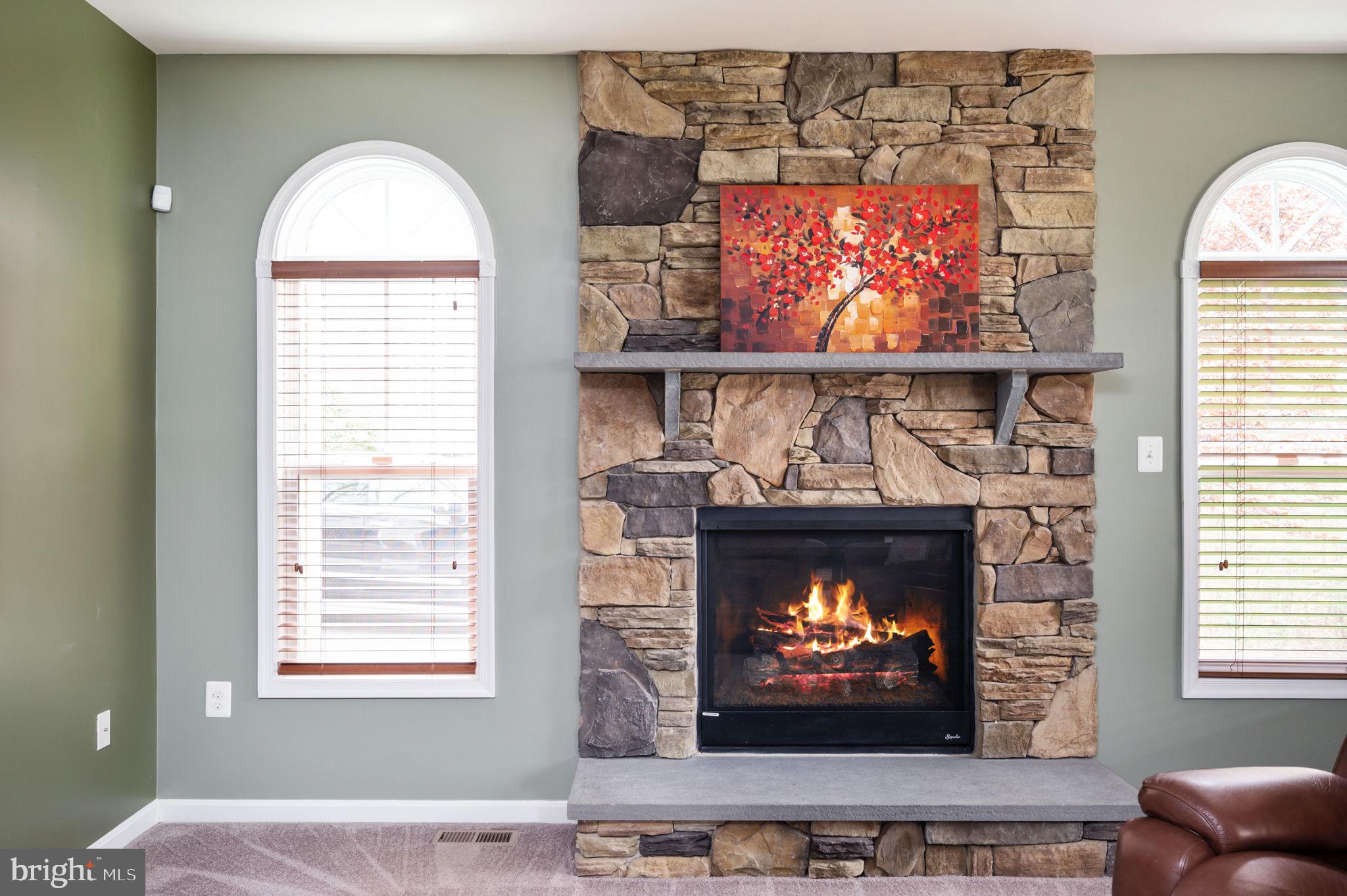 Living room with a burning fire in a large stone fireplace between arched windows.