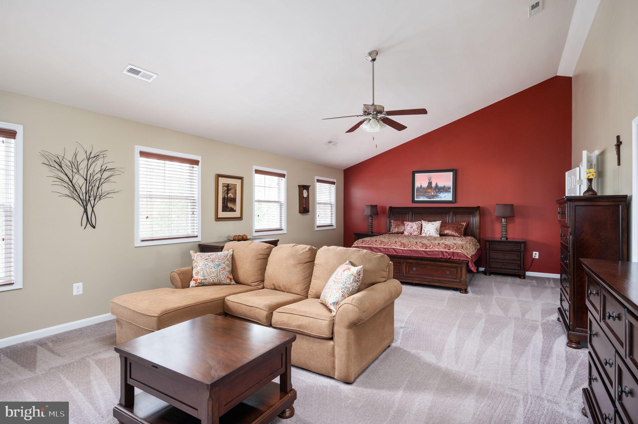 Furnished bedroom with a beige sectional sofa and dark wood bed against a red accent wall.