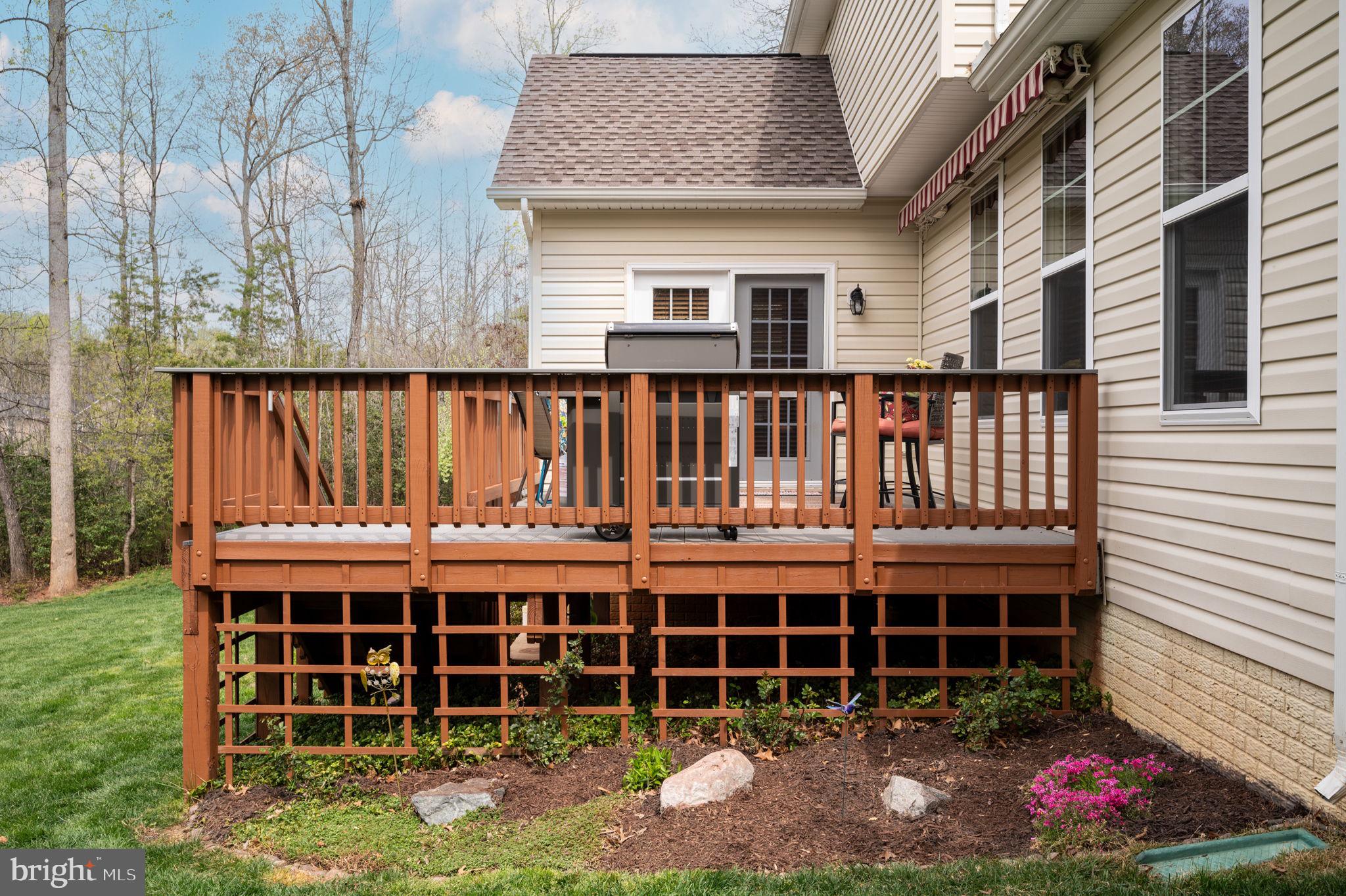 Raised wooden deck with a grill and patio chairs beside a landscaped garden.