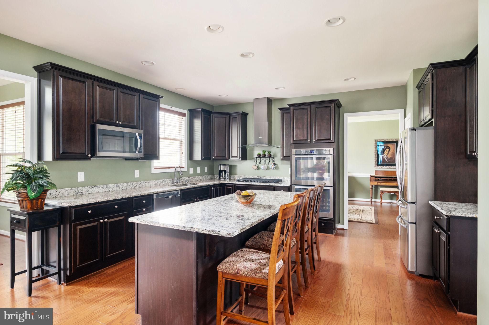 Kitchen with dark wood cabinets, granite island, wooden bar stools, and stainless steel appliances.