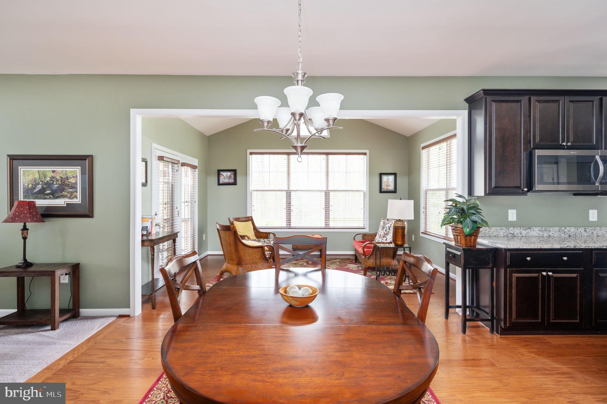 Dining room with a large oval wood table, chandelier, and an adjoining sitting area and kitchen.