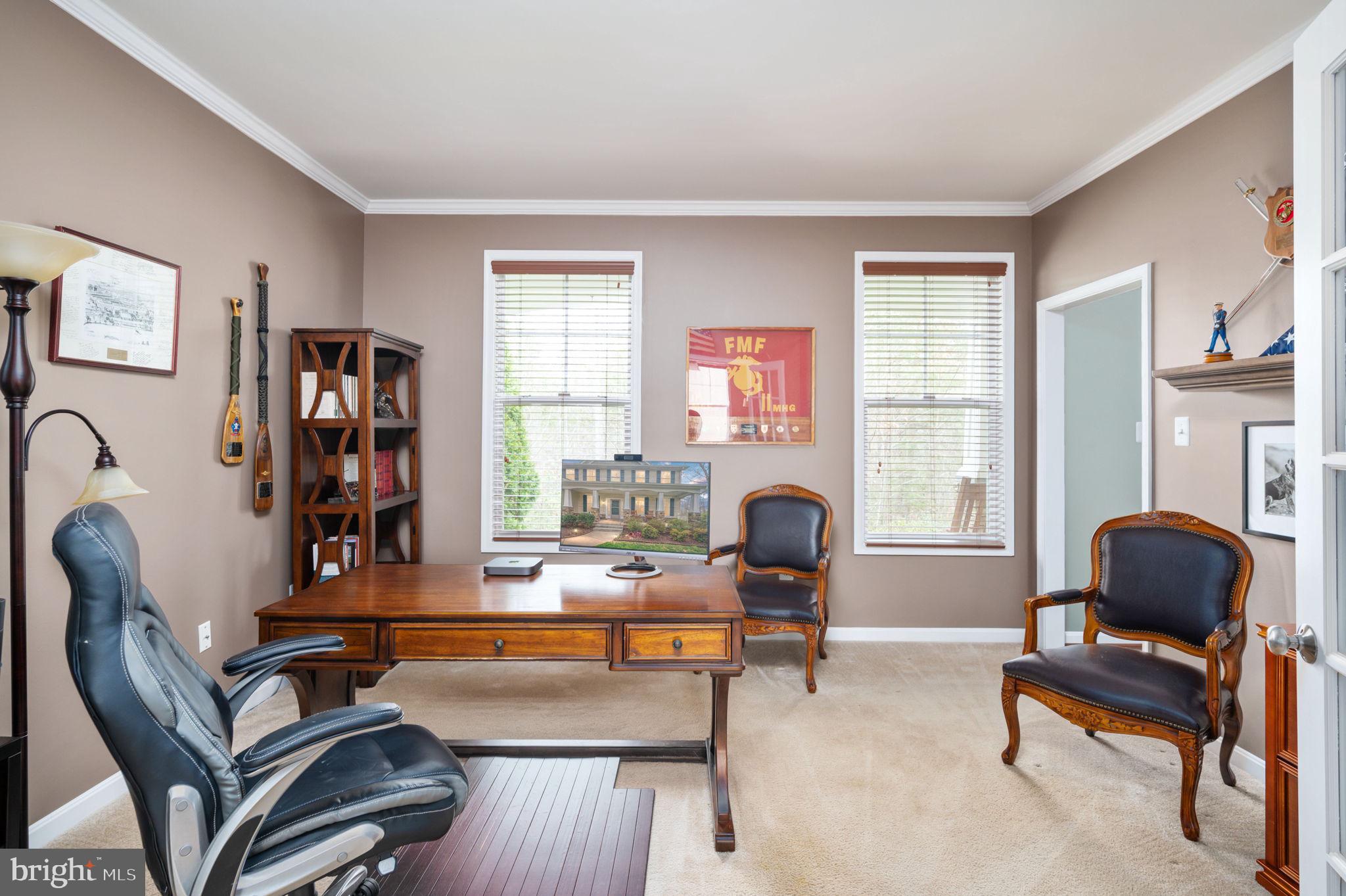 Furnished home office with a wooden desk, leather chairs, and Marine Corps display.