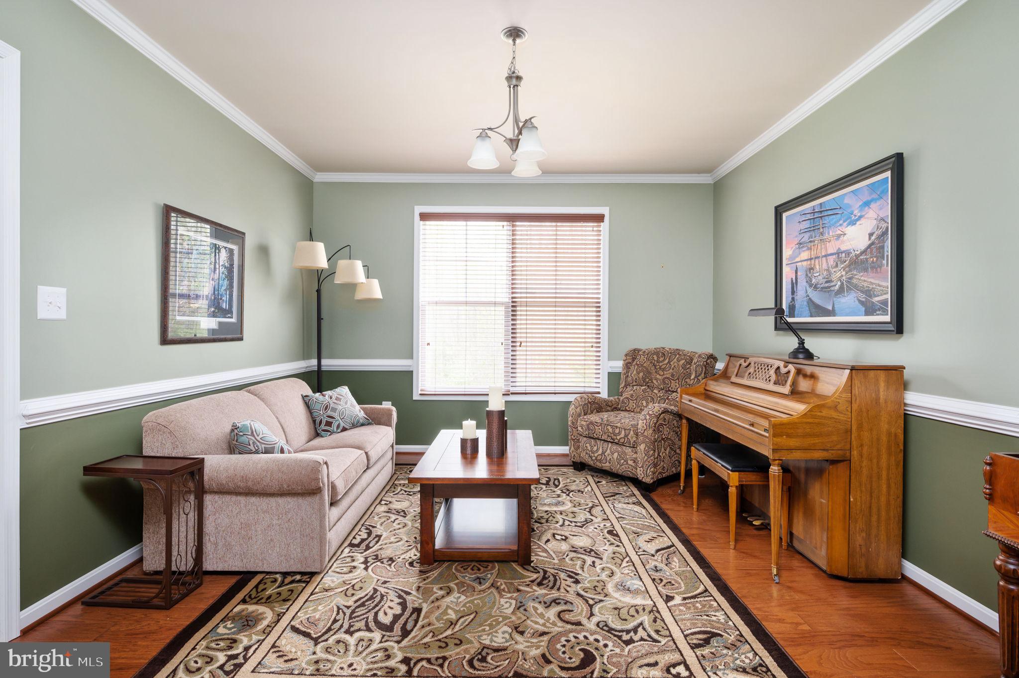 Living room with a beige sofa, patterned rug, and wooden upright piano.