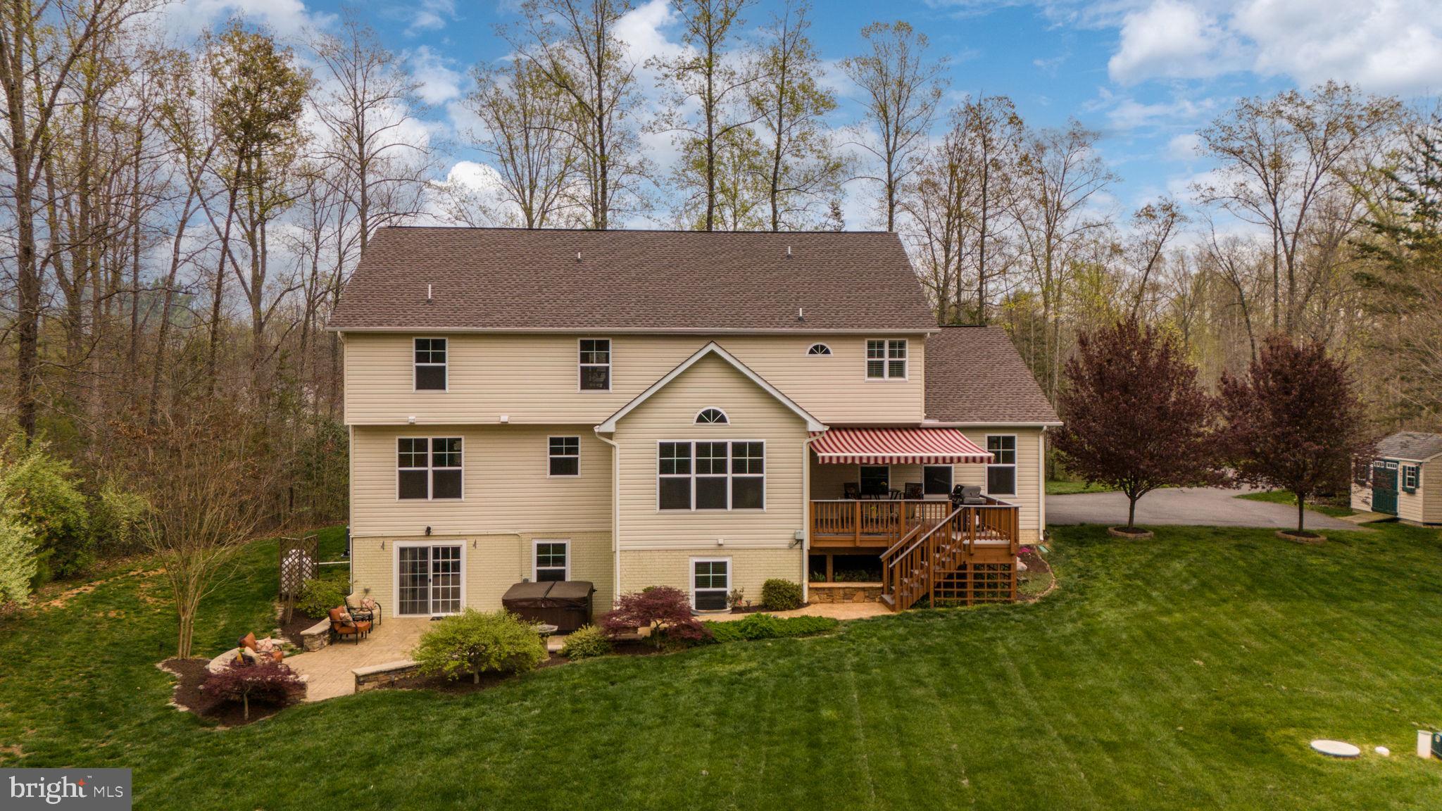 Rear of a beige multi-level house with a striped awning over the deck, patio, and broad lawn.