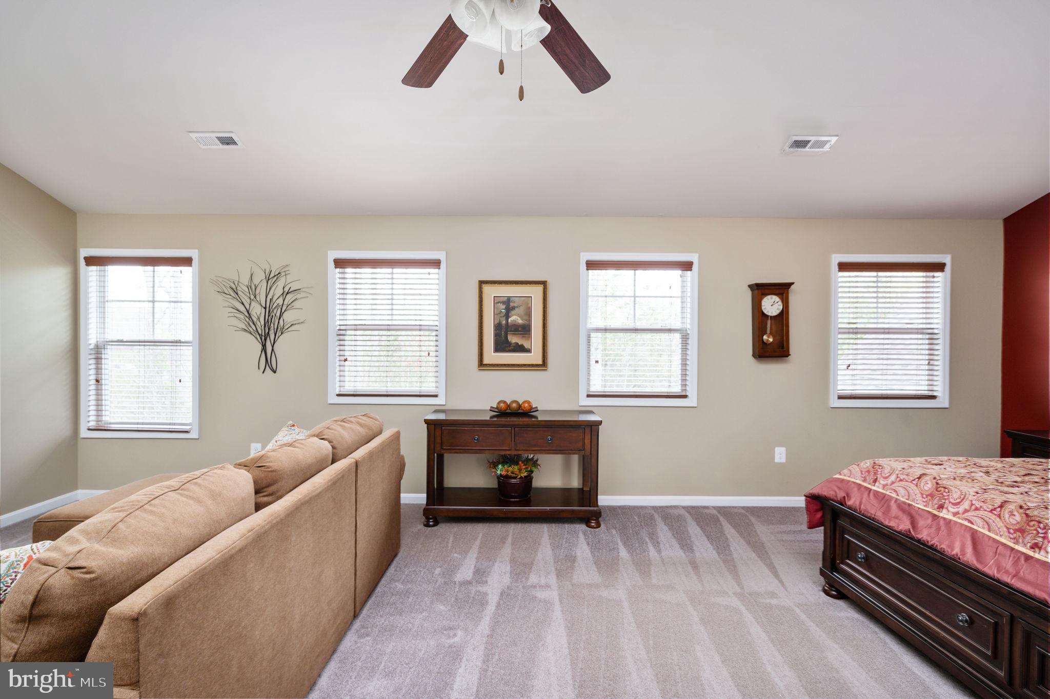 Furnished bedroom with a tan sofa, dark wood bed, and four windows with blinds.
