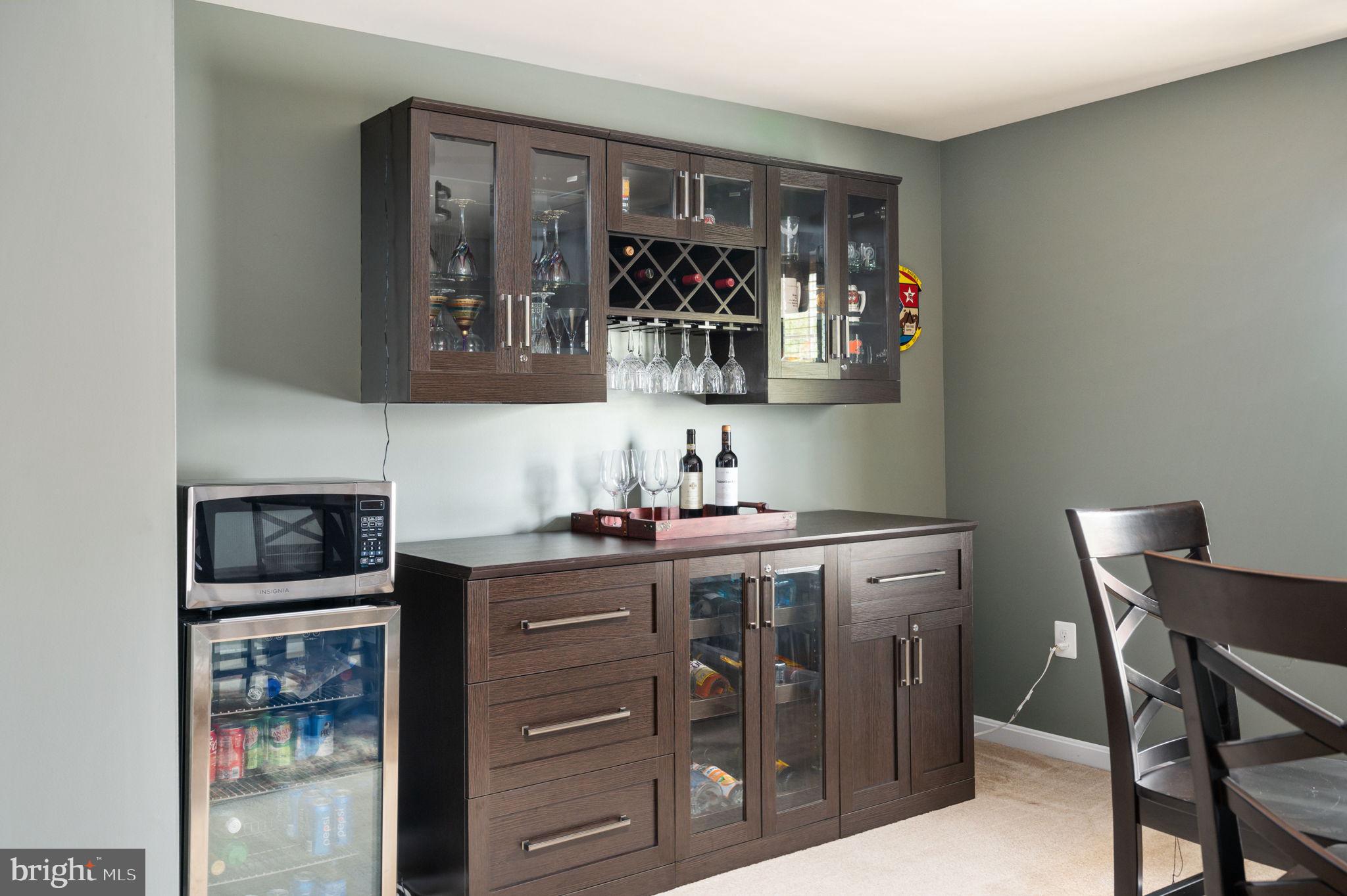 Home bar with dark wood cabinetry, wine storage, hanging stemware, and a beverage refrigerator.