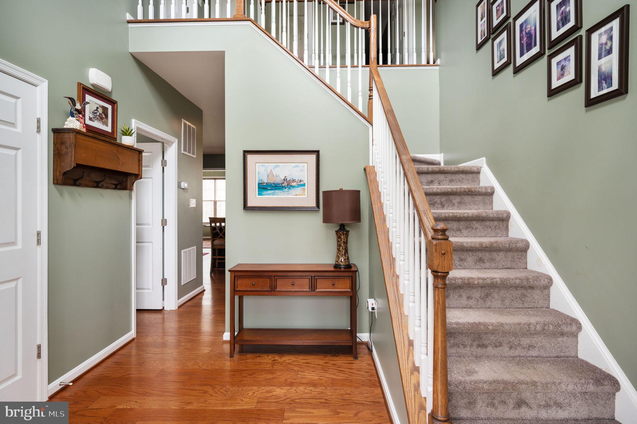 Foyer with carpeted staircase, wood handrail, hardwood floor, and console table beneath framed artwork.