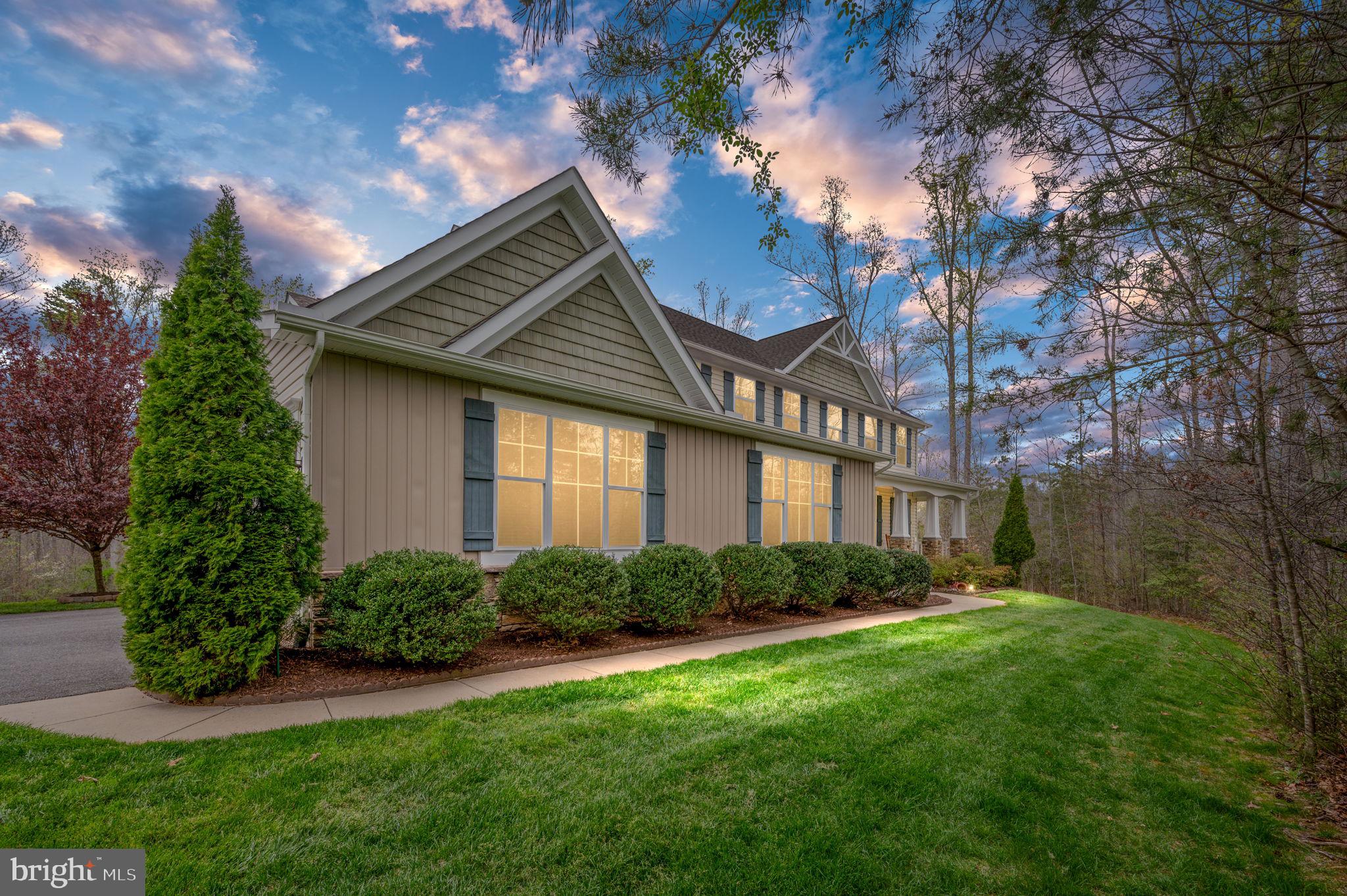 Two-story house with prominent gables, blue shutters, and a landscaped lawn at dusk.