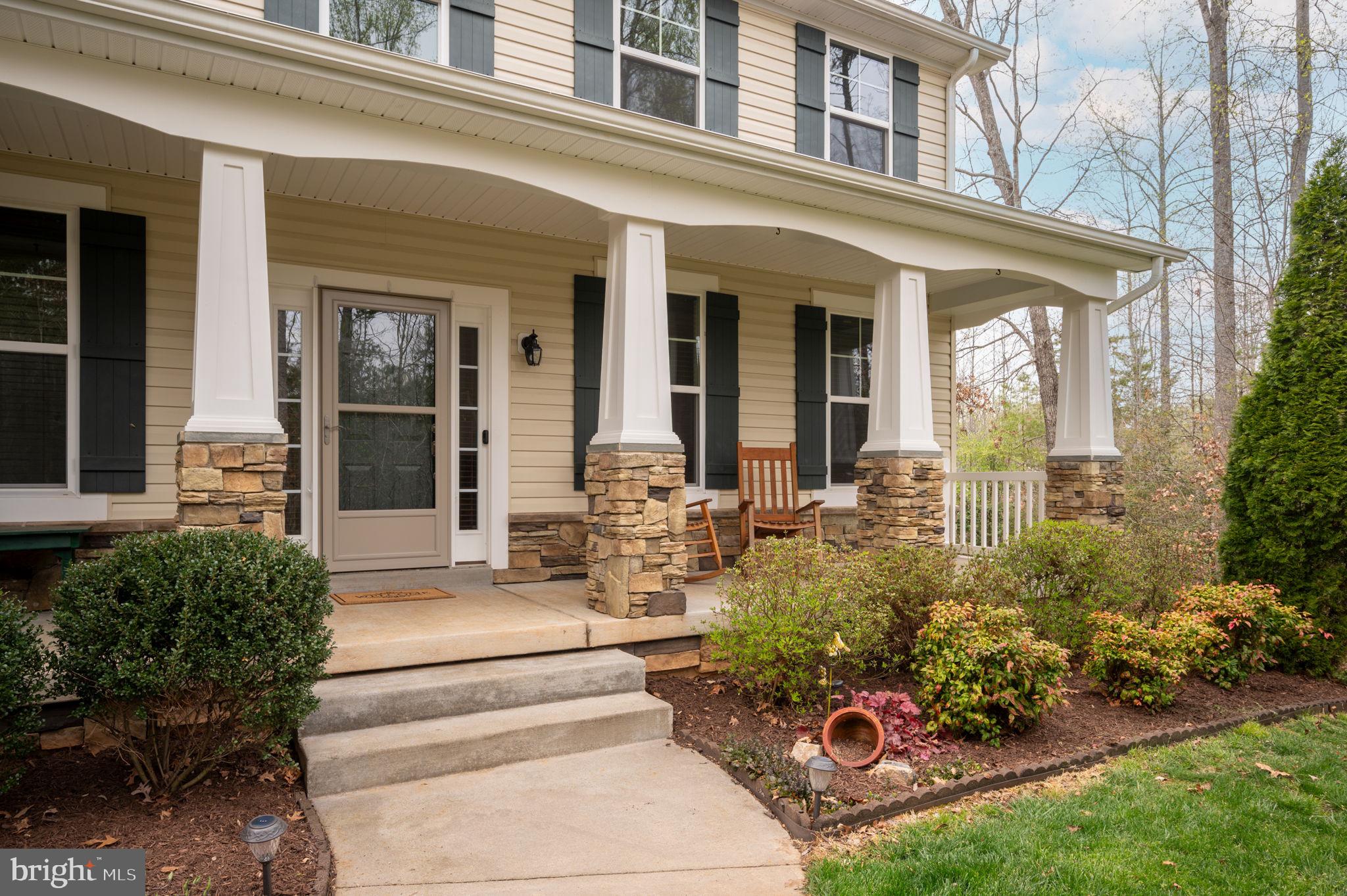 Home with a covered porch, stone-based columns, wooden chairs, and landscaped garden.