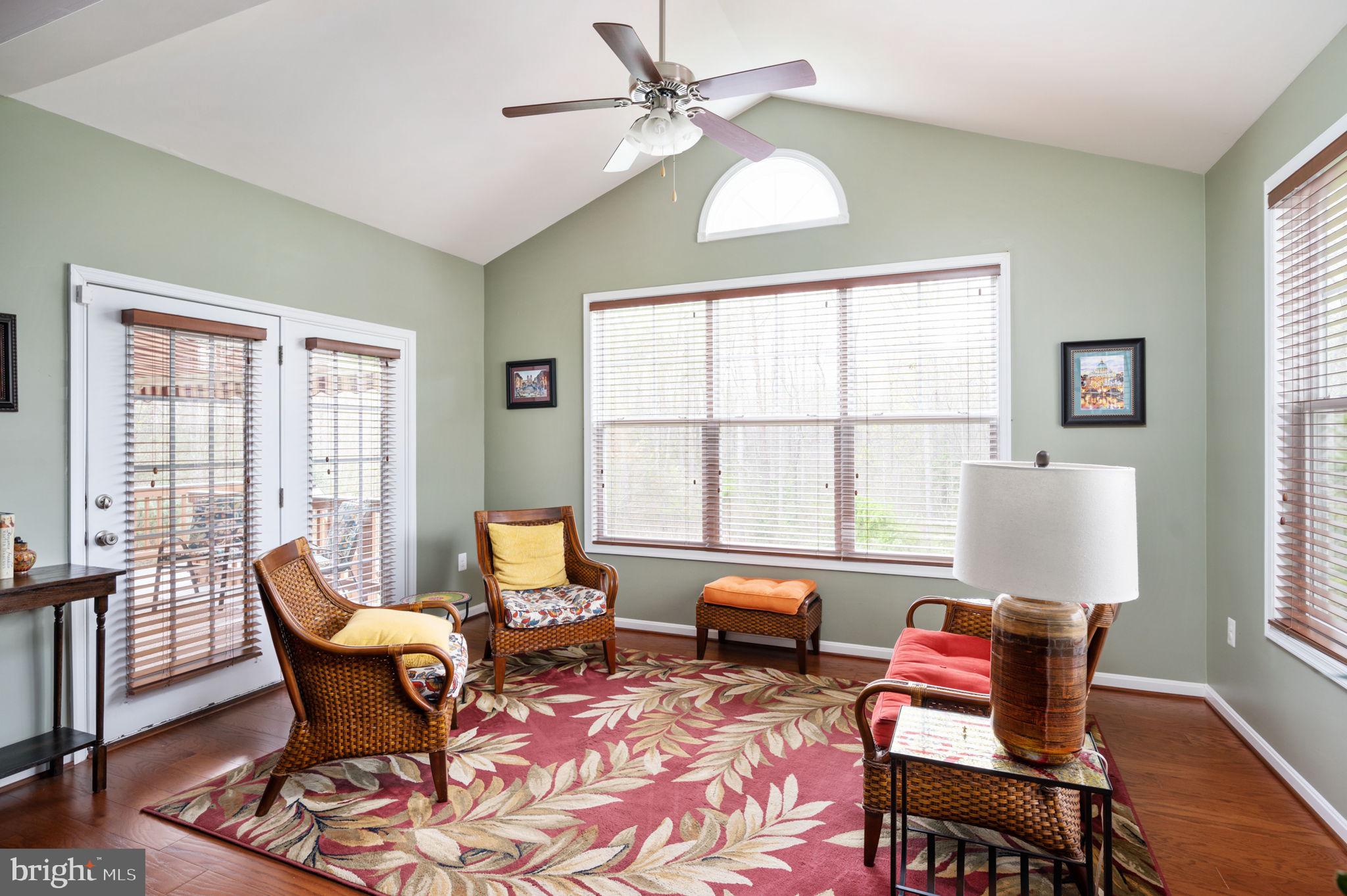 Furnished sitting room with wicker chairs, a floral rug, vaulted ceiling, and large windows.