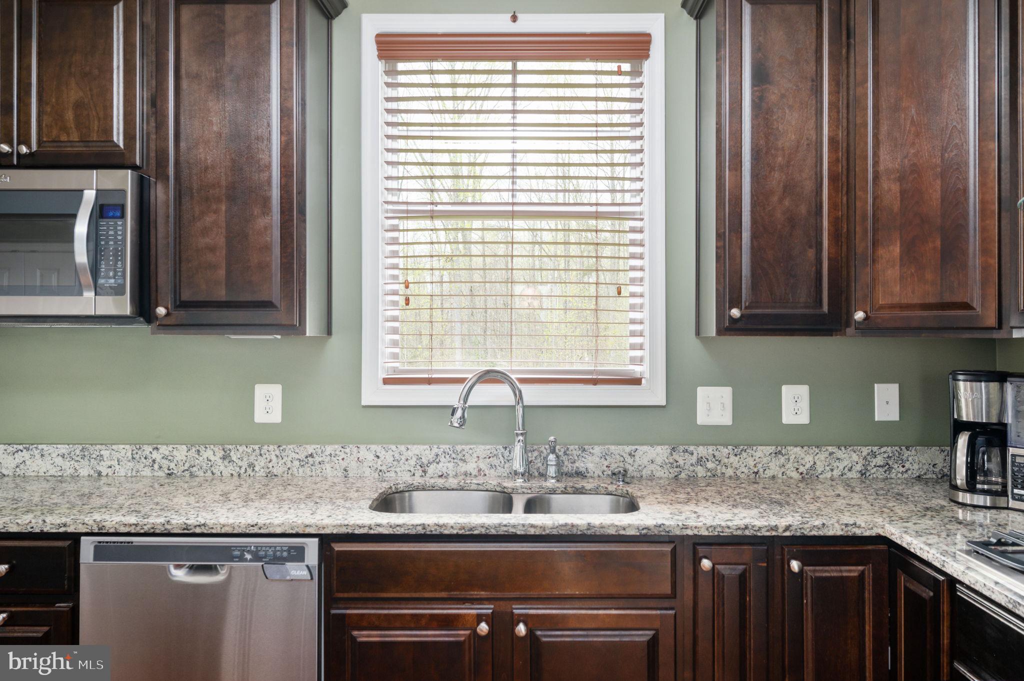 Kitchen sink beneath a window, with dark wood cabinets and speckled stone countertops.