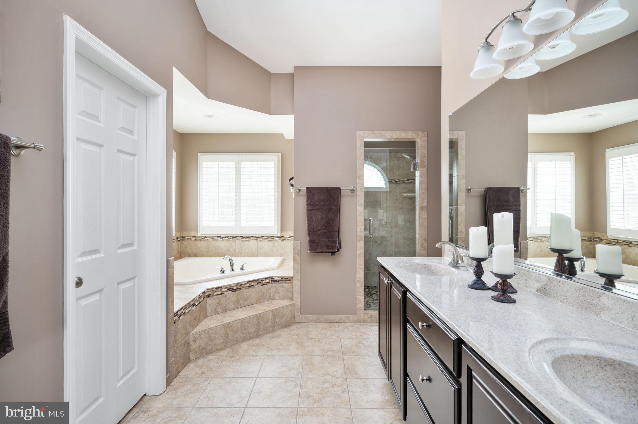 Primary bathroom with a long double-sink vanity, corner soaking tub, and tiled glass shower.