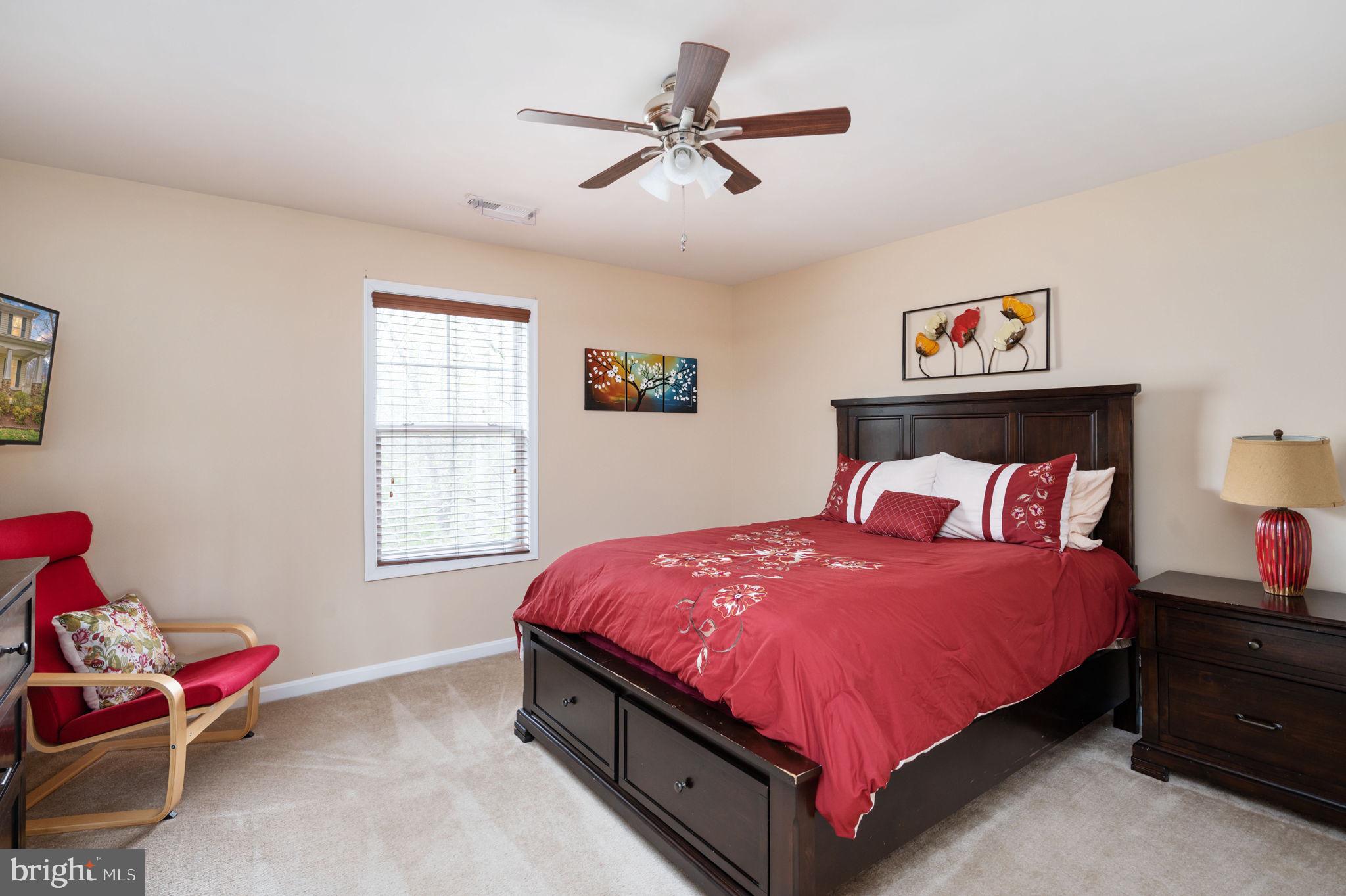 Bedroom with red floral bedding, dark wood furniture, and a red chair beside the window.