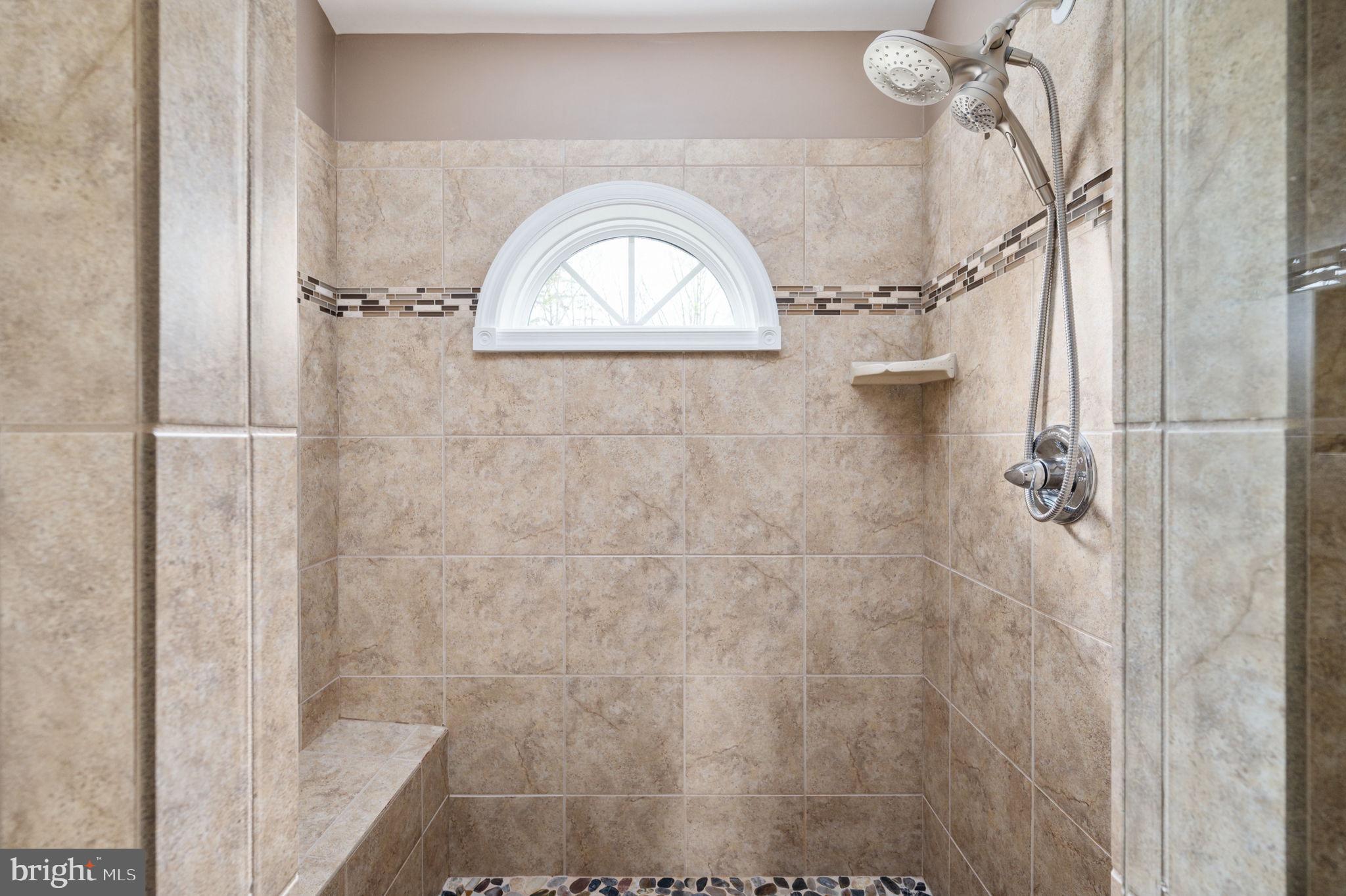 Walk-in shower with beige tile, an arched window, mosaic accent band, and built-in bench.