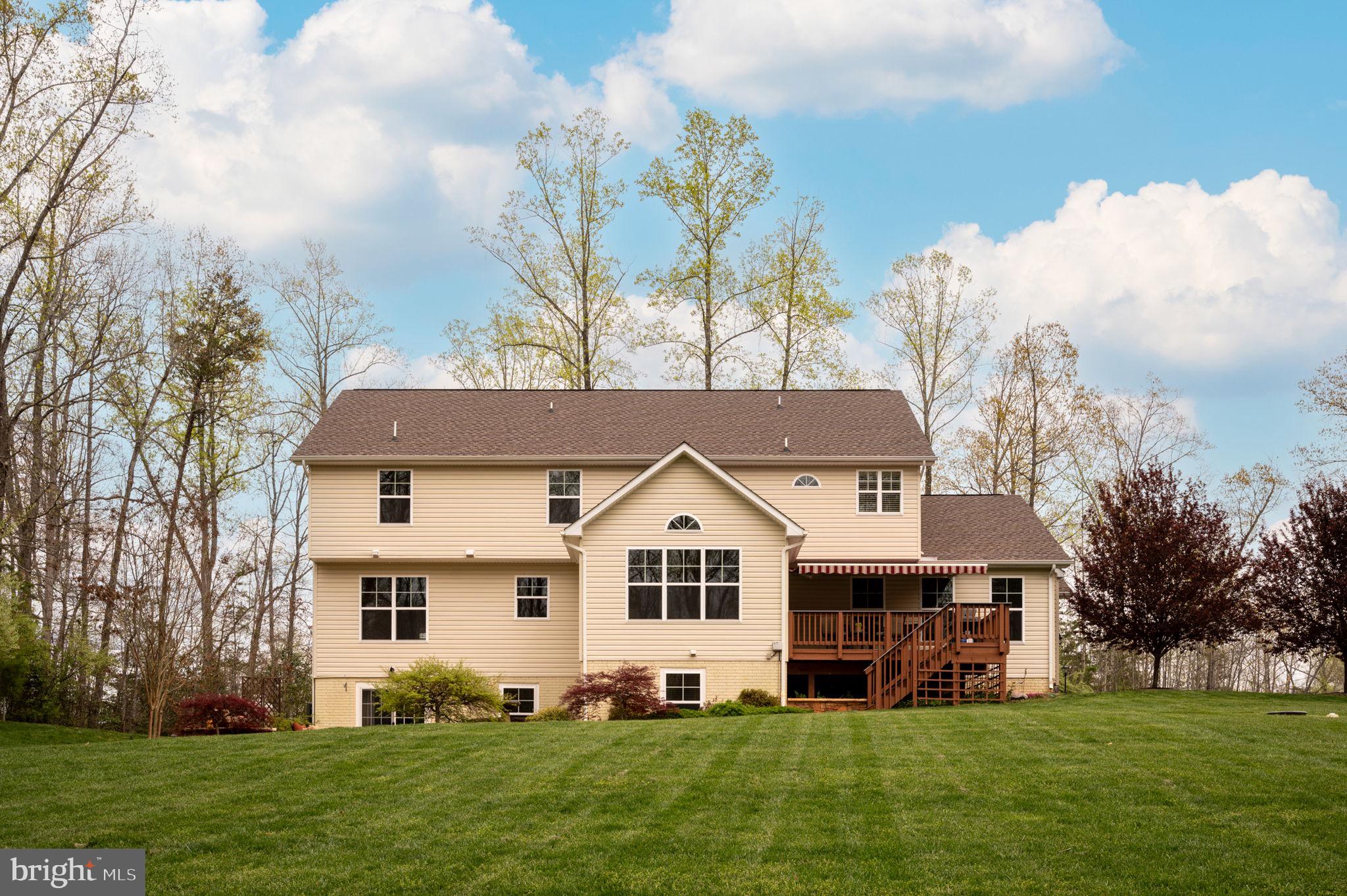 Rear of a beige two-story house with a wooden deck and stairs overlooking a broad lawn.