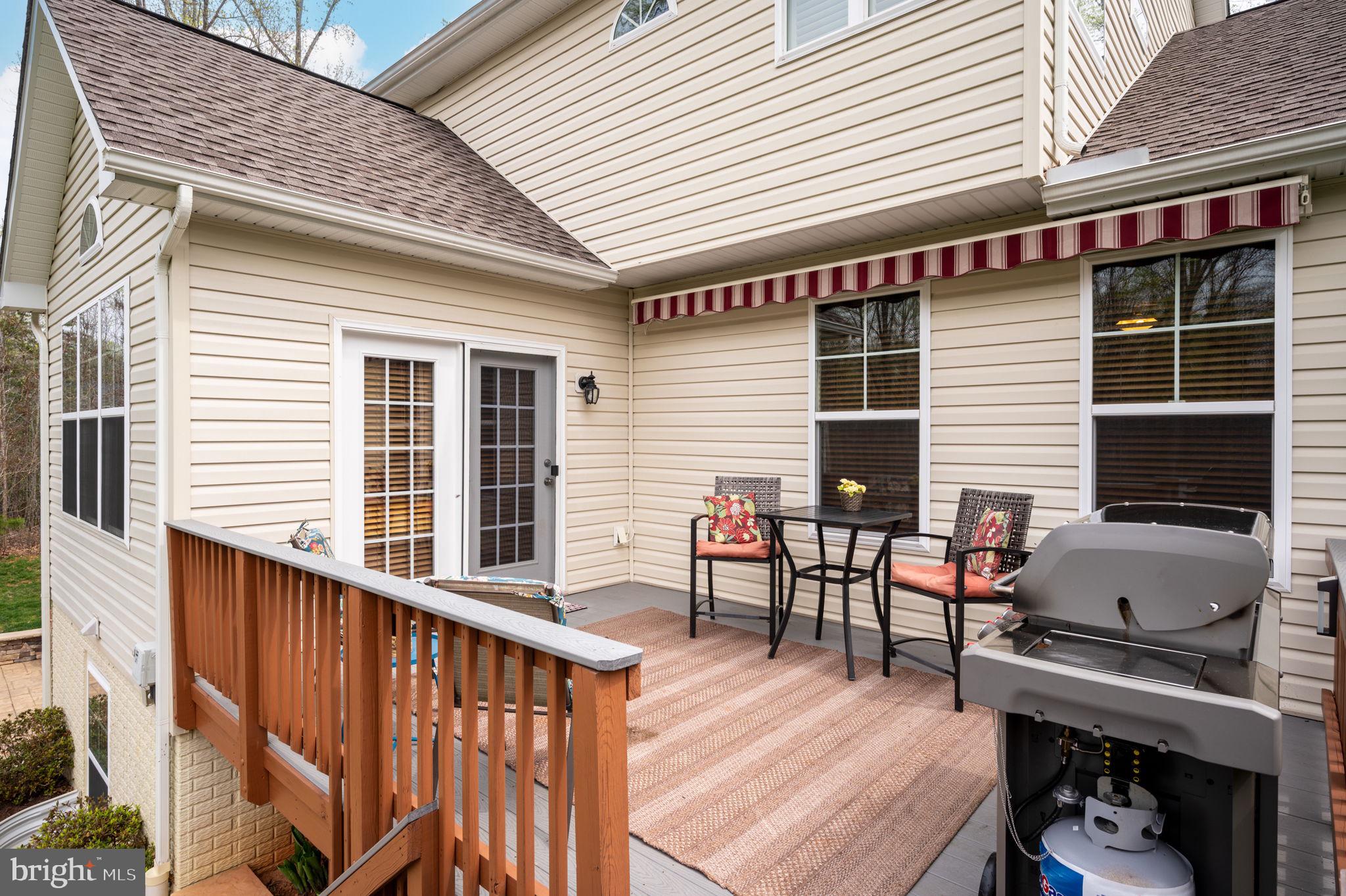 Raised deck with striped awning, outdoor dining set, rug, and large gas grill.