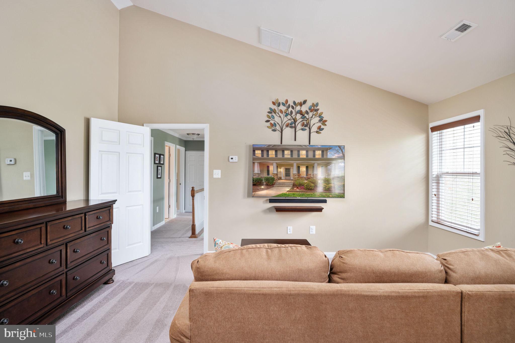 Living room with tan sectional, dark wood dresser, and wall-mounted television.